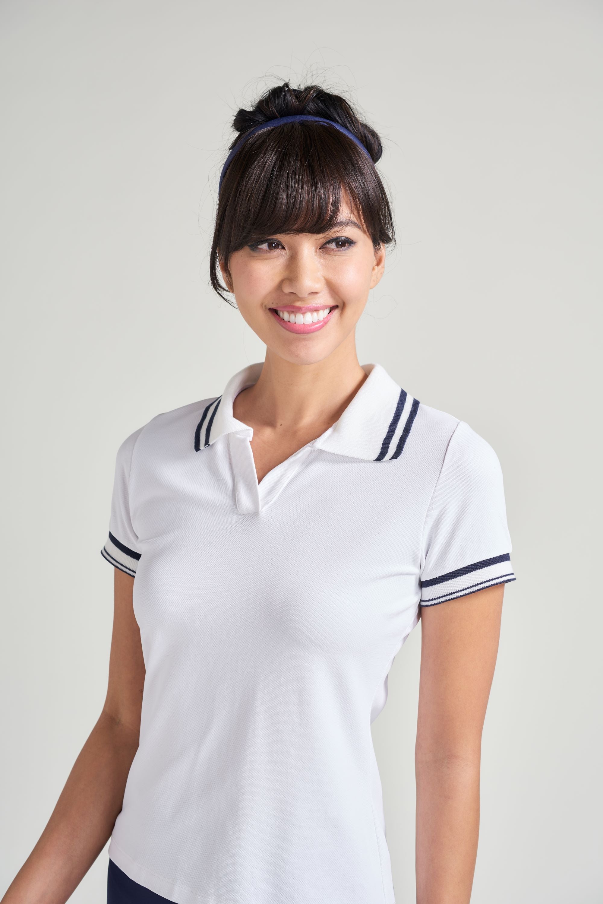 A woman tennis player wearing a white collared polo with navy and white trim along collar and sleeves.