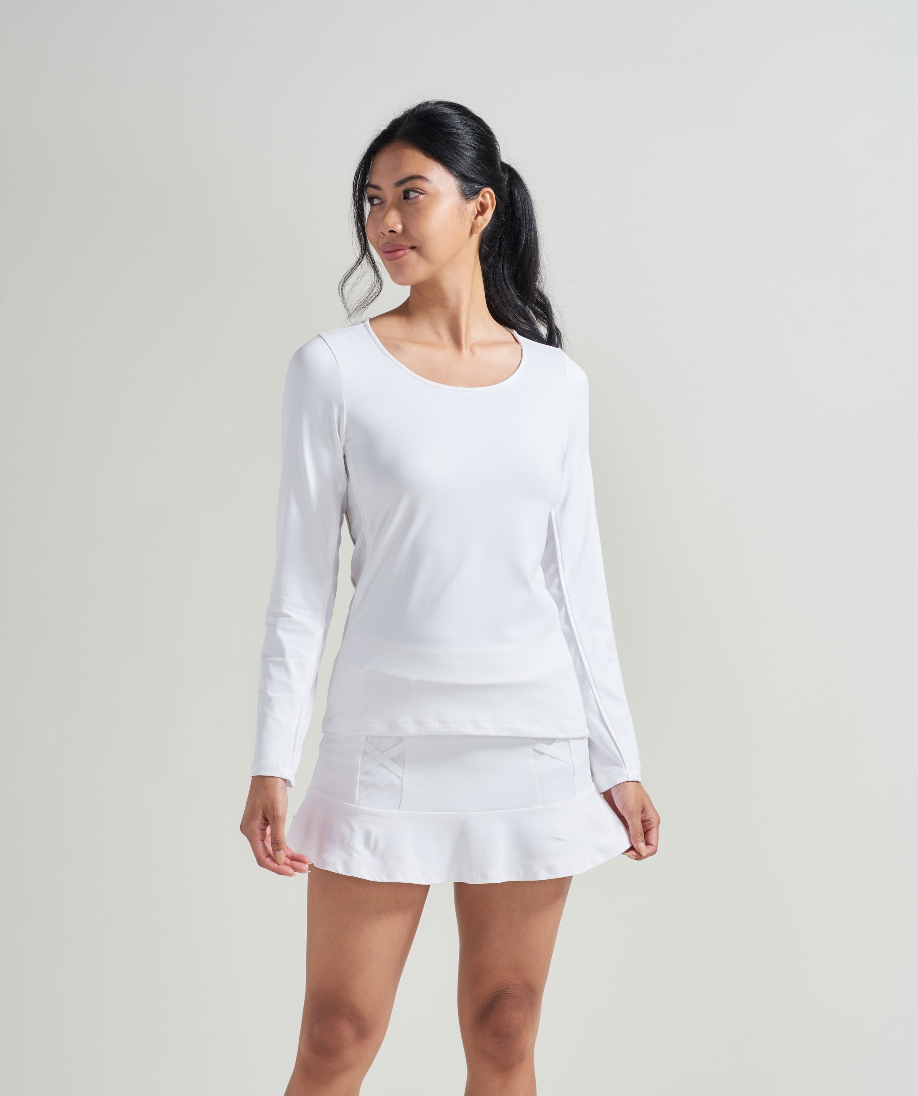 Women's white tennis long sleeve shirt with scoop neck. Woman is also wearing a white tennis skort with white trim.