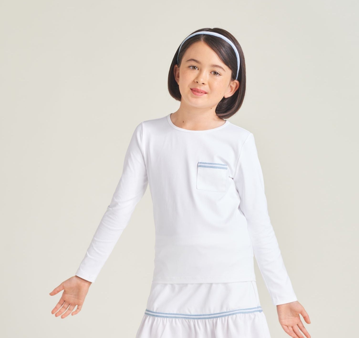 Tennis athlete wearing unisex kids' long sleeve tennis t-shirt in white with blue and white trim on shirt pocket.