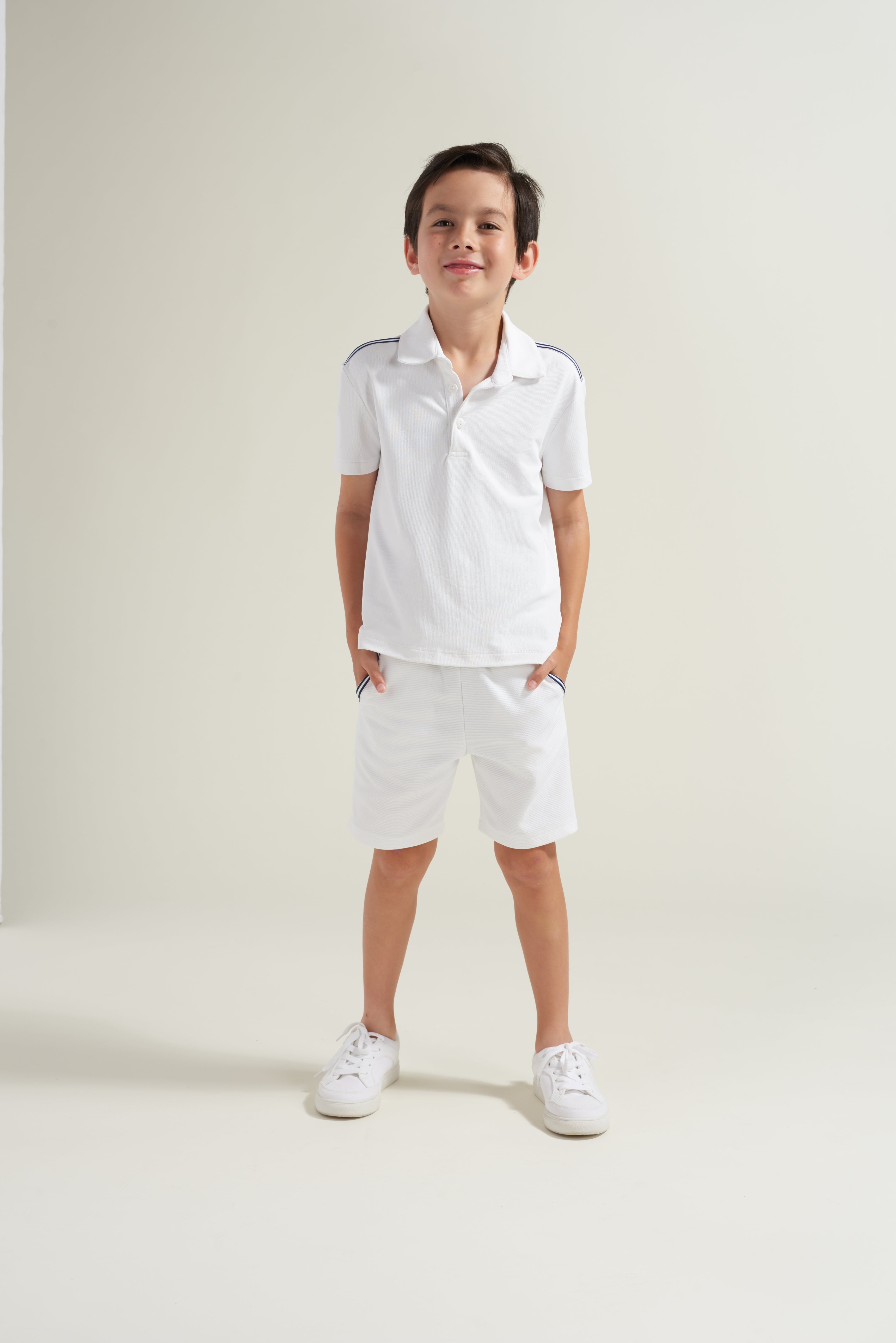 Youth tennis player wearing a white tennis uniform with navy and white accent trim.