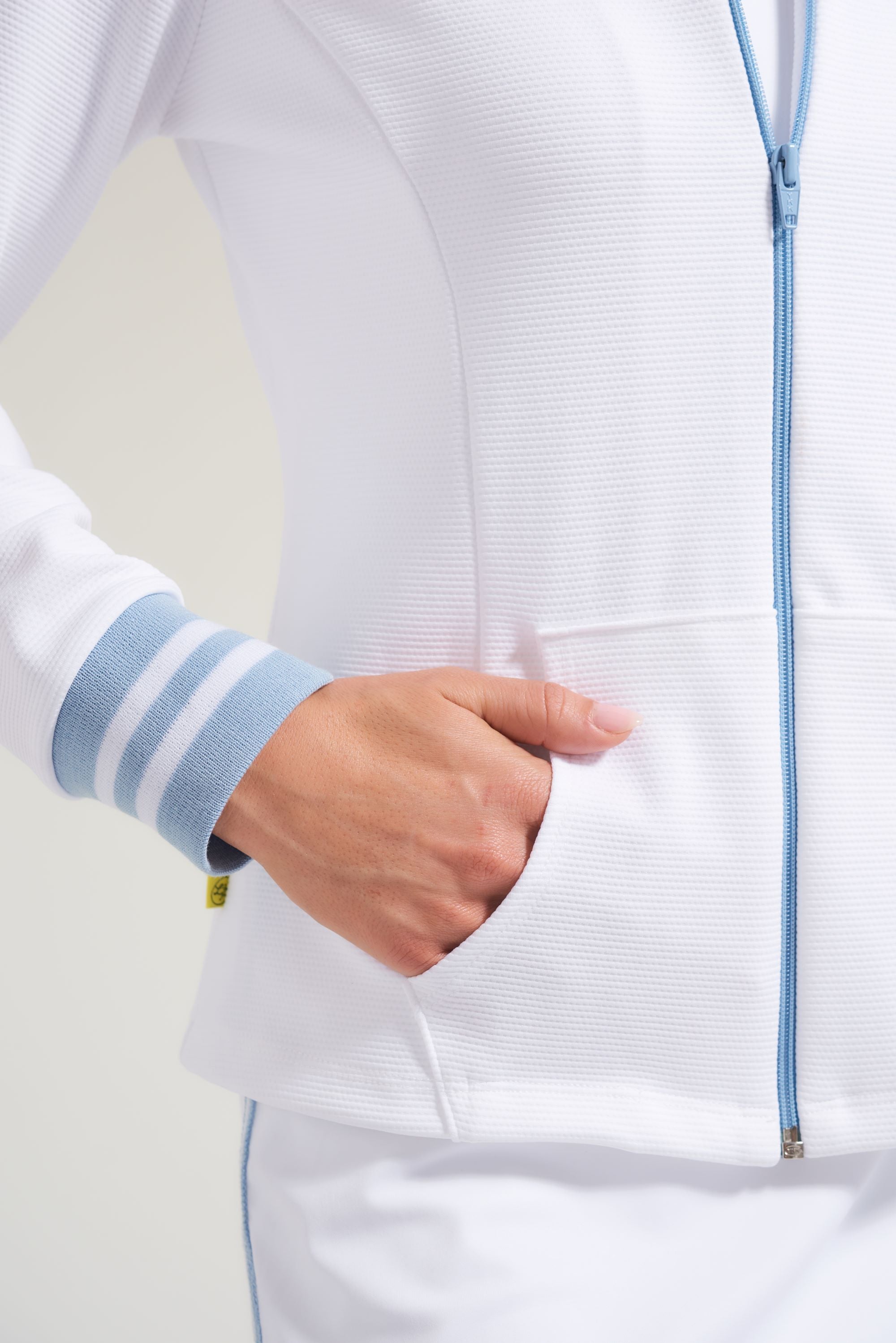 Detail picture of white women's tennis jacket with blue zipper and striped blue and white ribbed cuffs on sleeve.