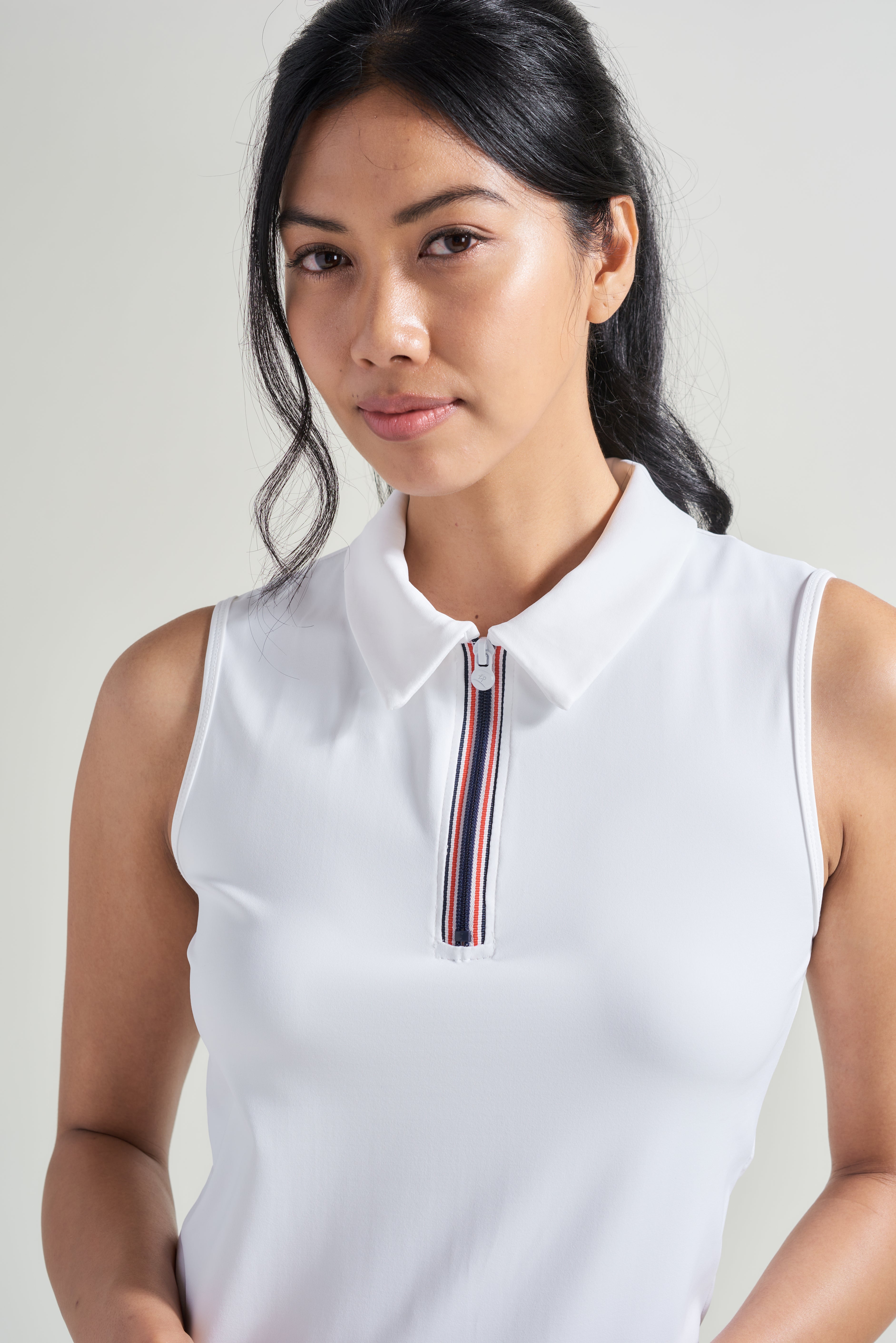 A detail shot of women's tennis polo shirt with red and navy zipper down neckline.