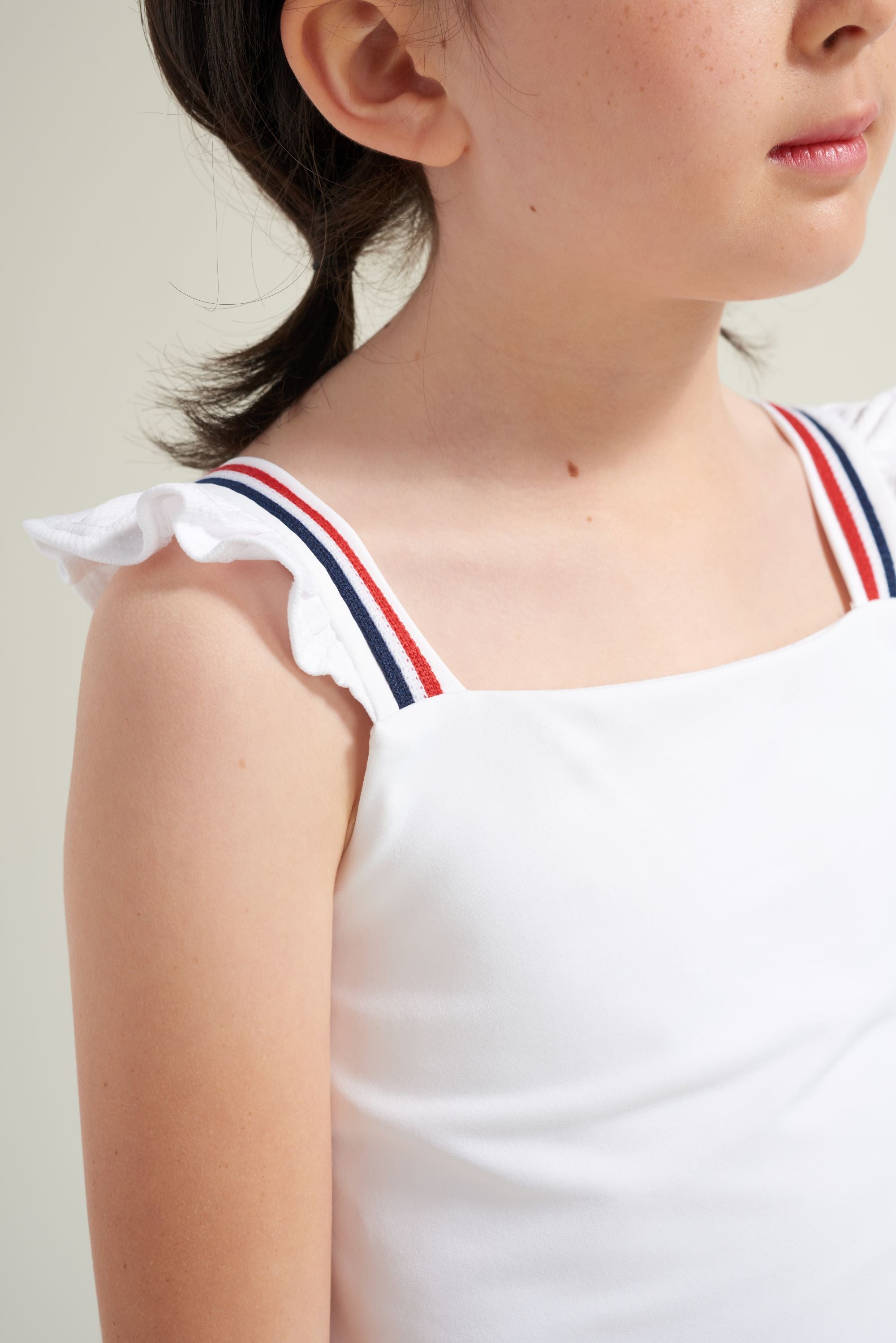 Detail view of white tennis sleeveless tank with red and navy trim on straps for kids.