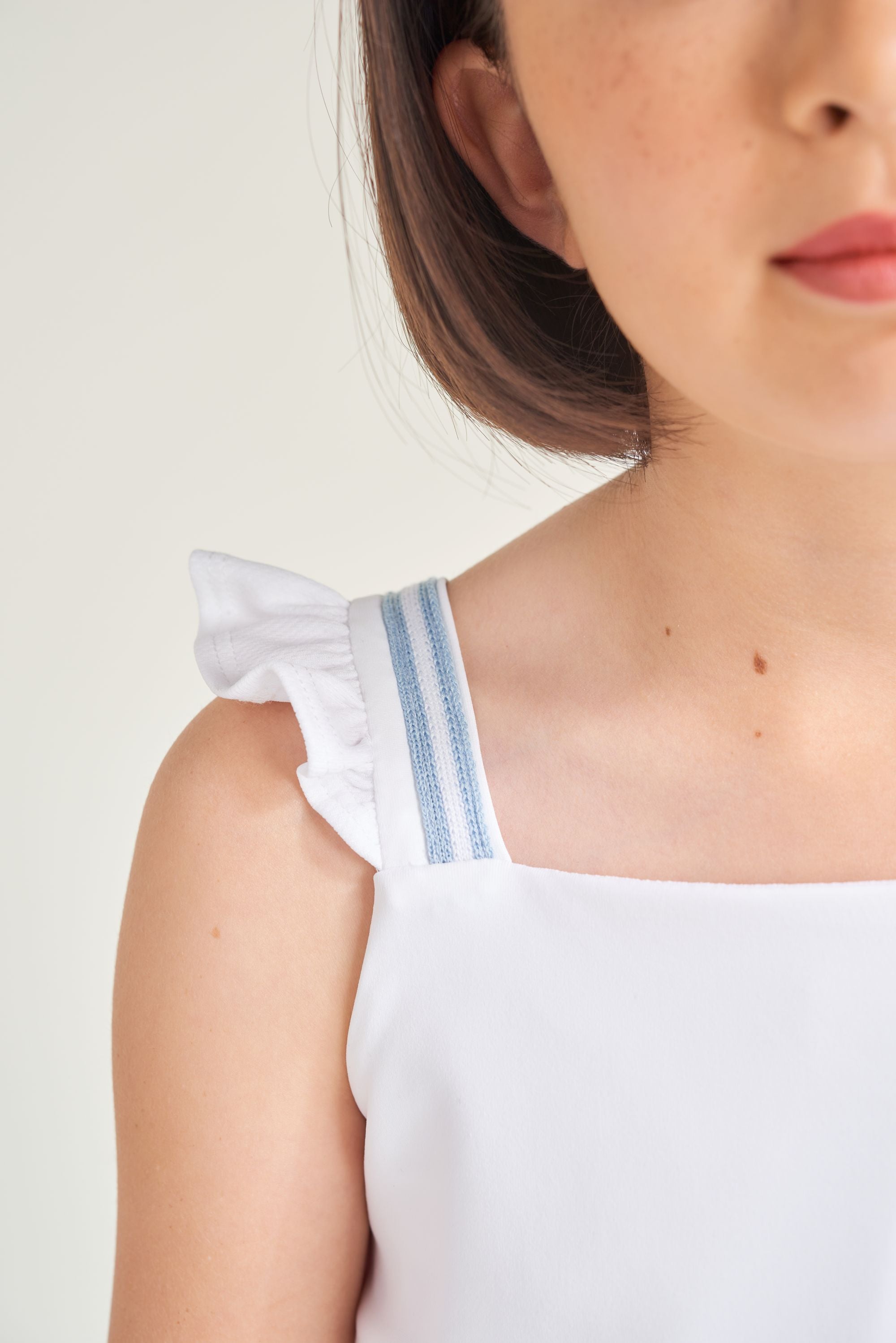 Detail picture of a white tennis t-shirt with knitted blue and white trim on strap and ruffle along strap.