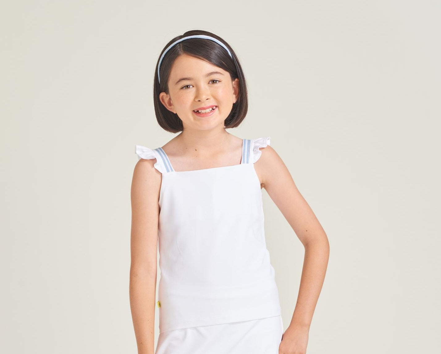 Girl tennis player is wearing a white tennis tank top with ruffles and blue and white trim on the straps.