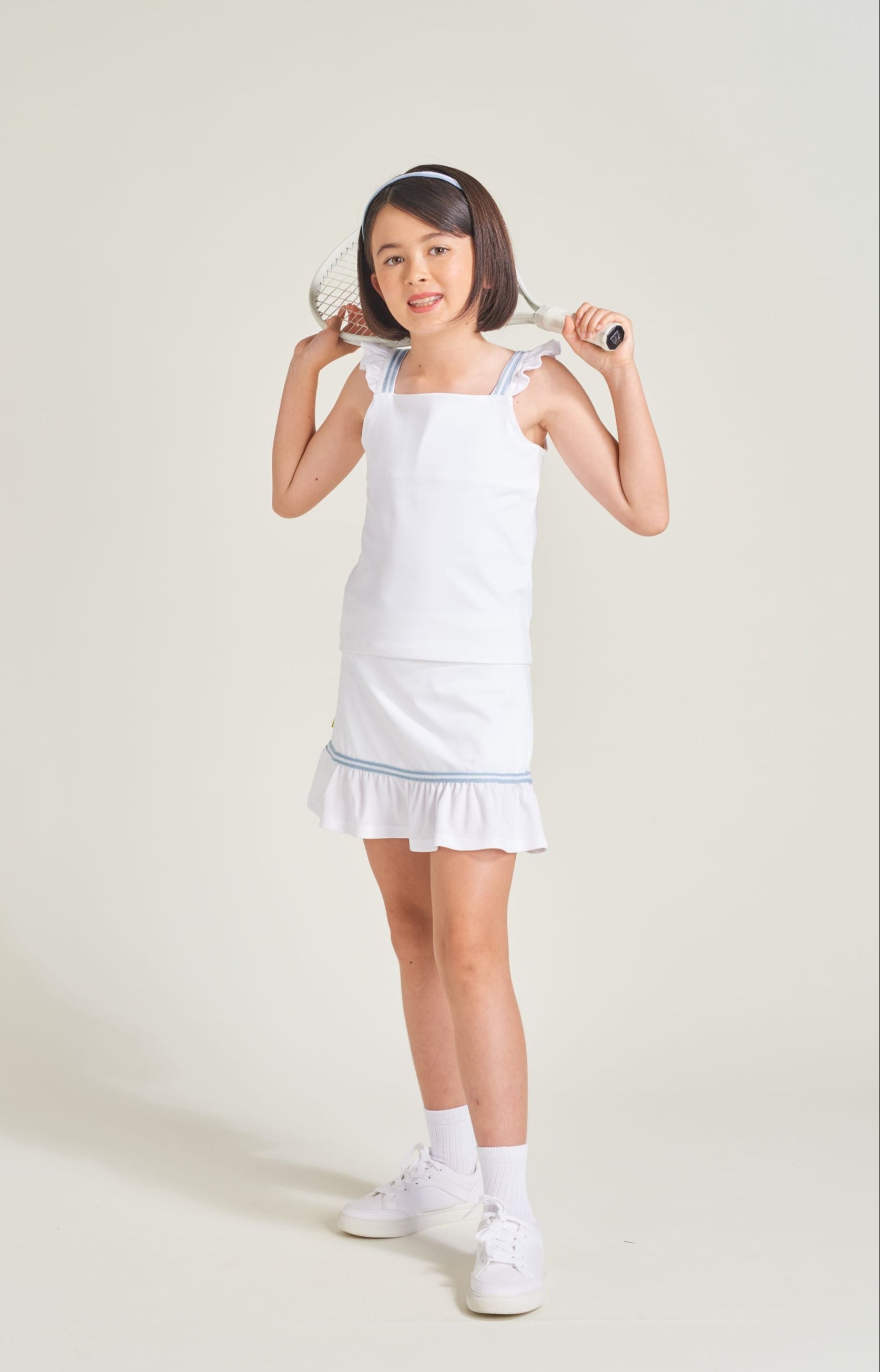 Youth girls tennis player wearing a white tennis t-shirt and a matching white tennis skort with blue and white trim.