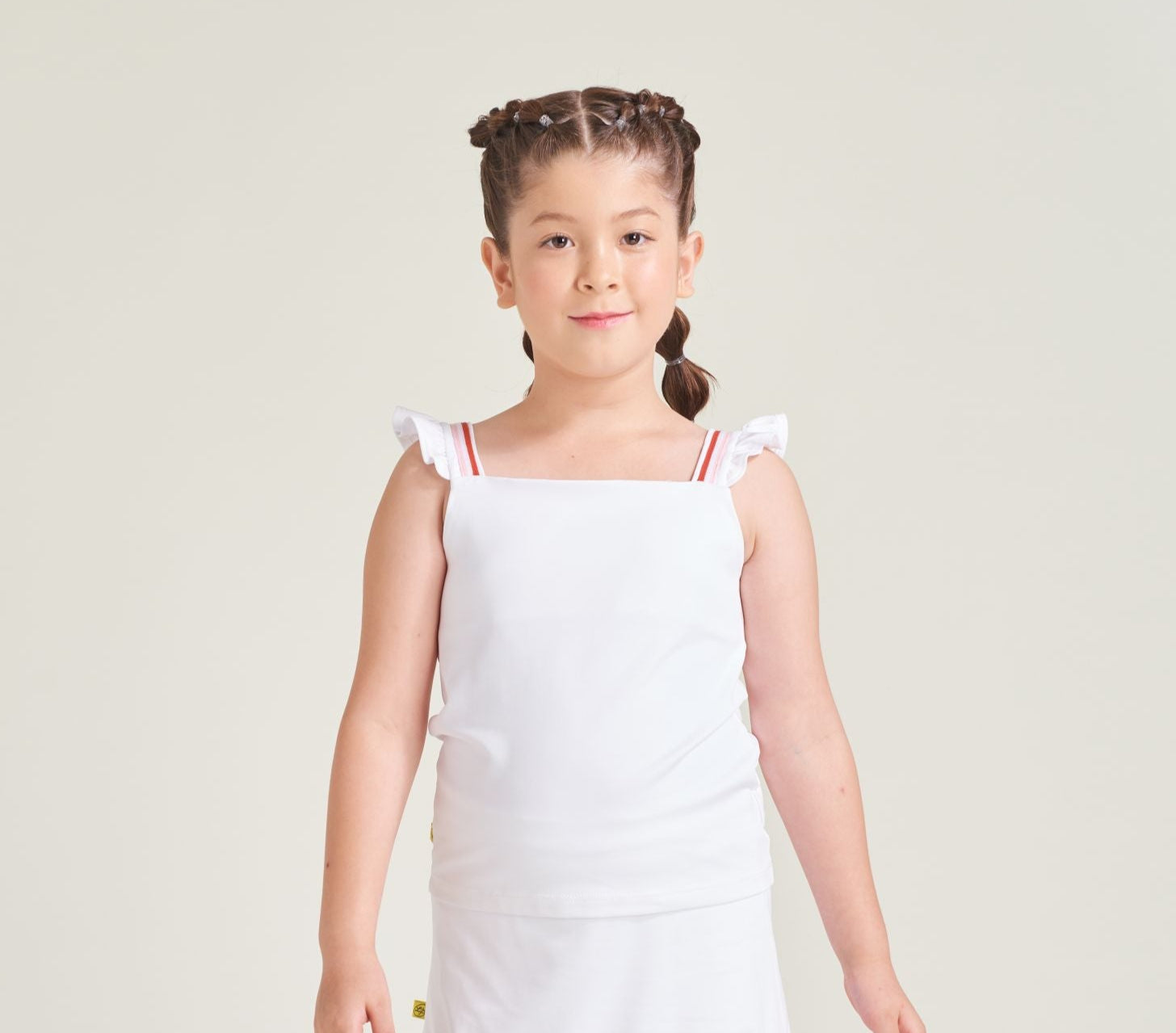 Youth girl tennis athlete is wearing a white tennis tank top with ruffles and red and pink trim on the straps.