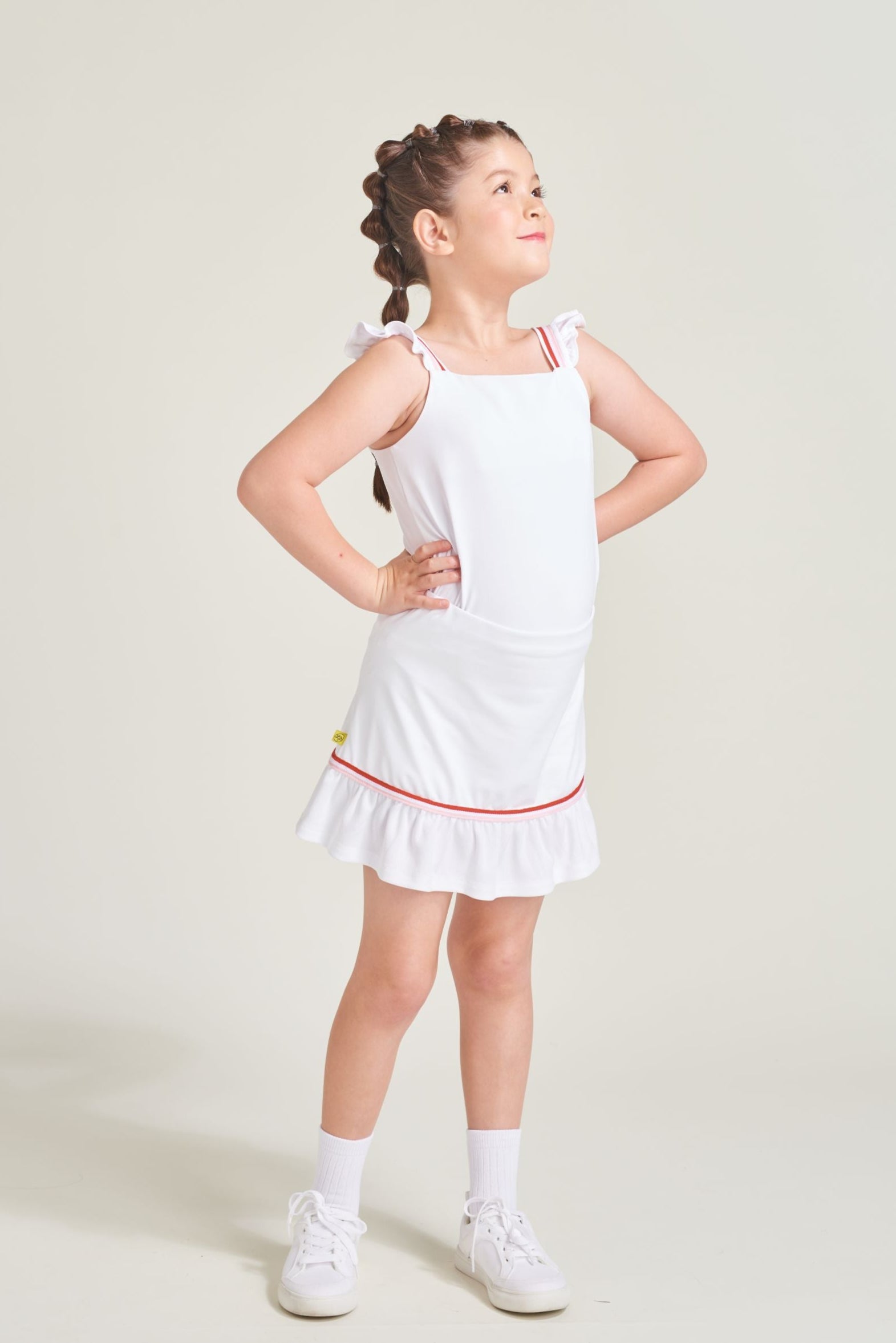 Girl tennis player has a white matching tennis set on. Girl is wearing a girls' tennis tank top with red and pink straps and a matching skort with red and pink trim along shirring.