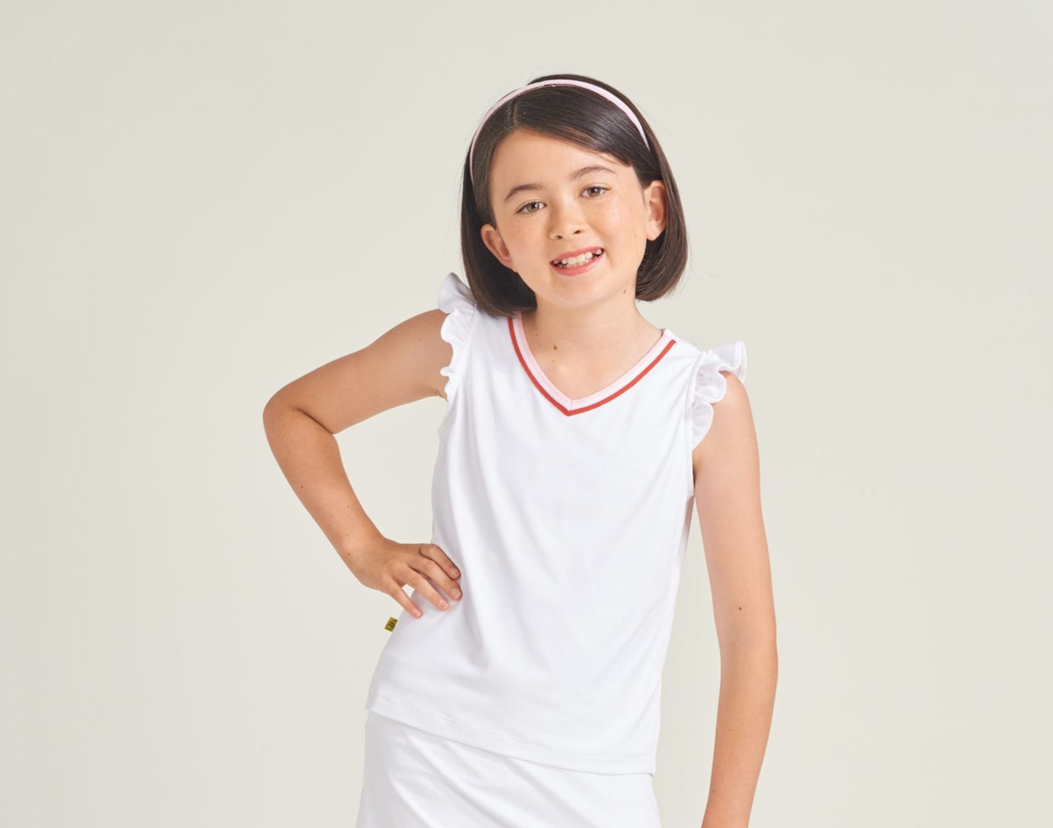 Girls tennis athlete is wearing a white tennis t-shirt with a v-neck line adorned with red and pink knitted trim.