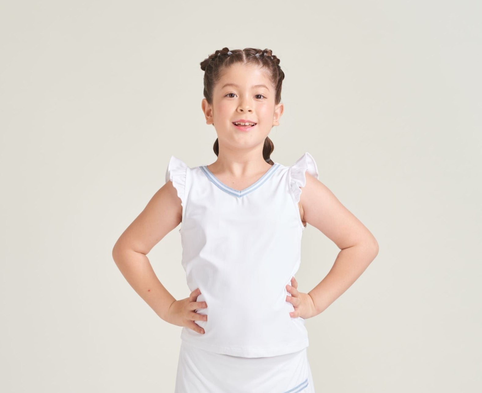 Youth girl tennis player wearing a white tennis tank top with ruffle sleeves and blue and white knitted trim on the neckline.