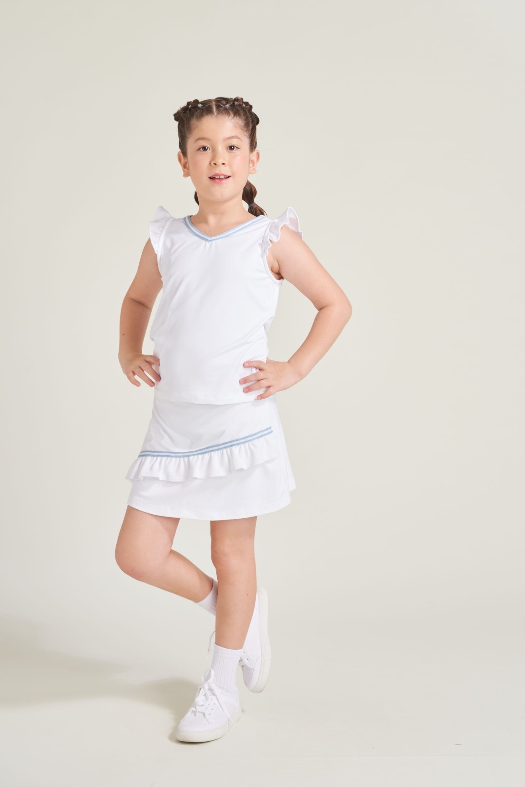 Girls tennis player is wearing a white tennis skort with blue and white trim across the front. Girl is also wearing a matching white top with blue and white trim along neckline.
