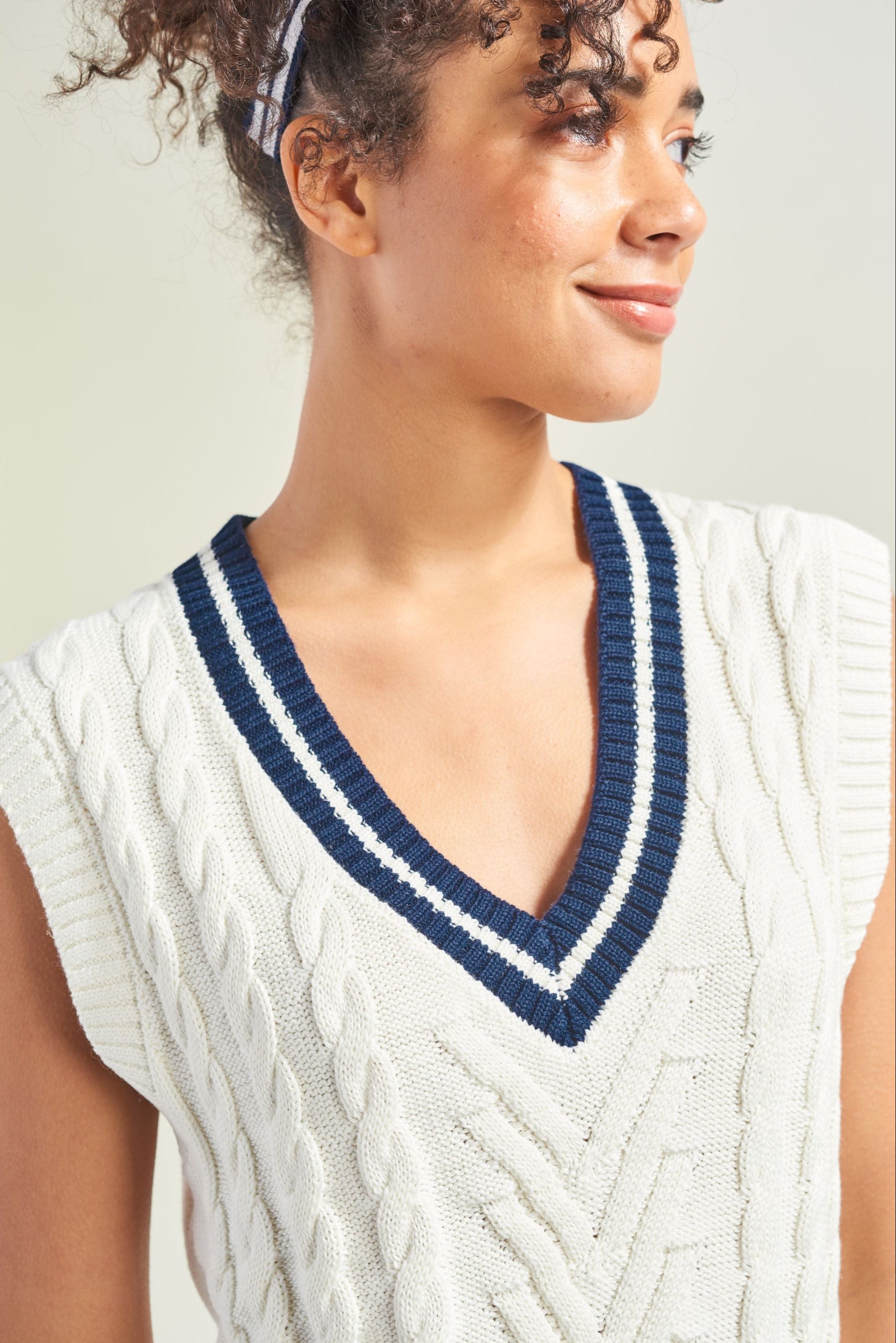 Woman wearing a white sleeveless knitted top with blue trim against a neutral background