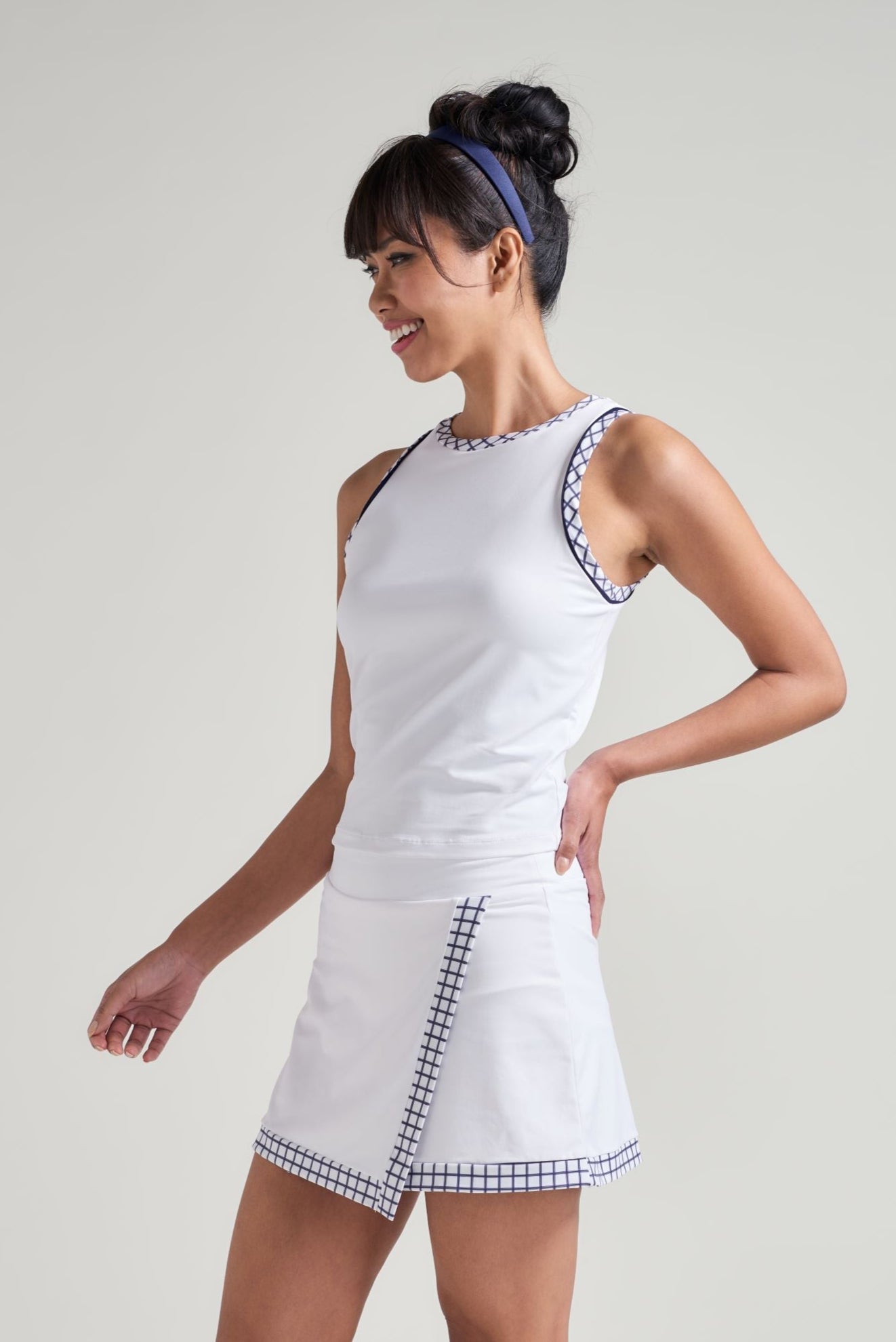 Side view of tennis player wearing tennis skort for women in white with navy and white checkered print along wrap hem.