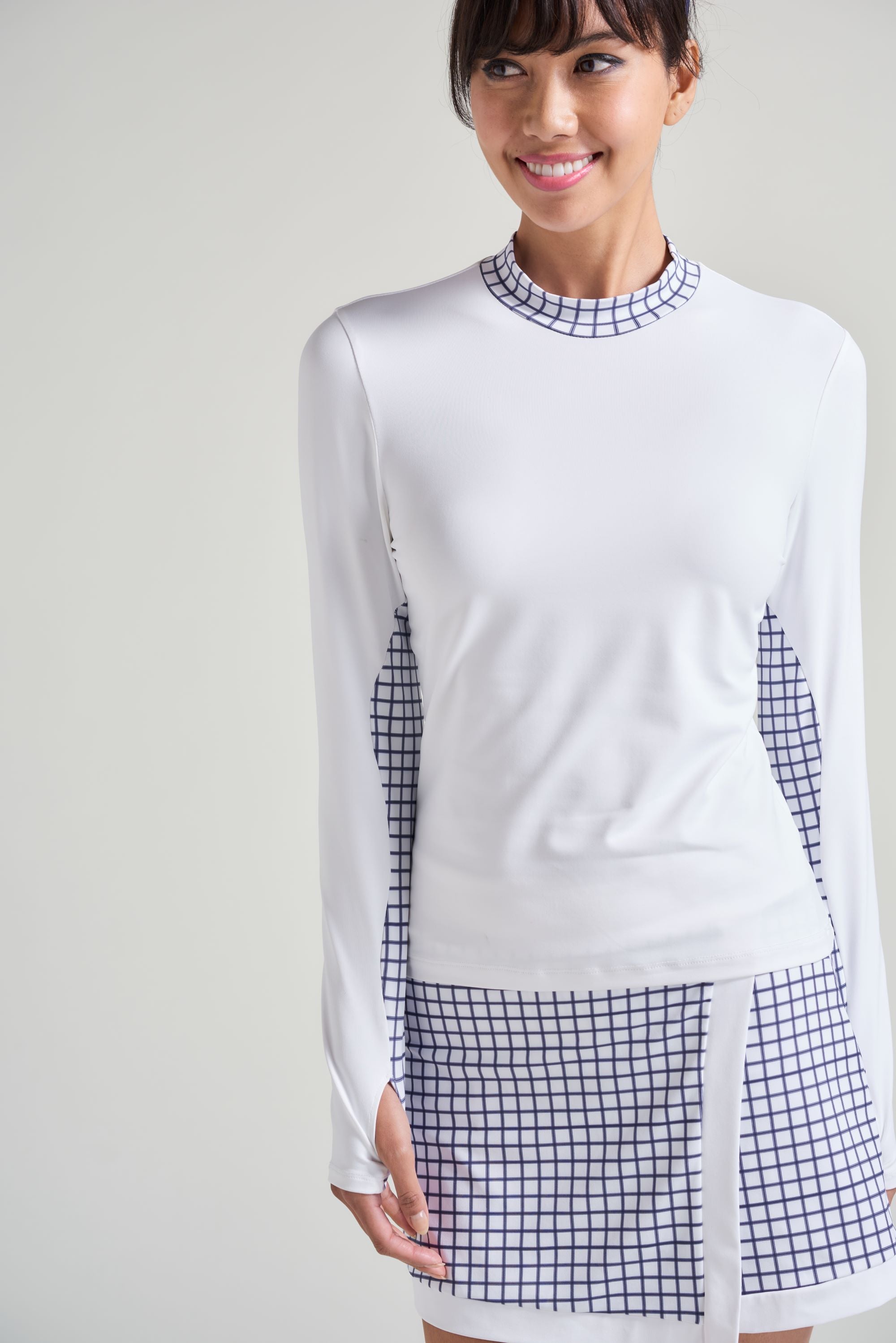 Women's tennis player in white tennis long sleeve shirt with white and navy checkered print accent and matching skort.
