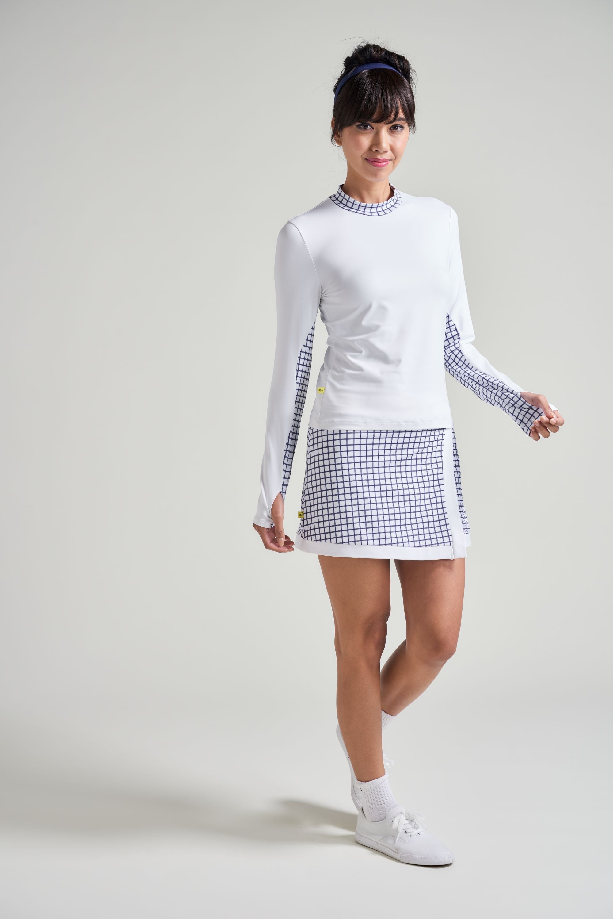 Women's tennis player wearing white tennis shirt with navy checkered print and matching tennis skort.