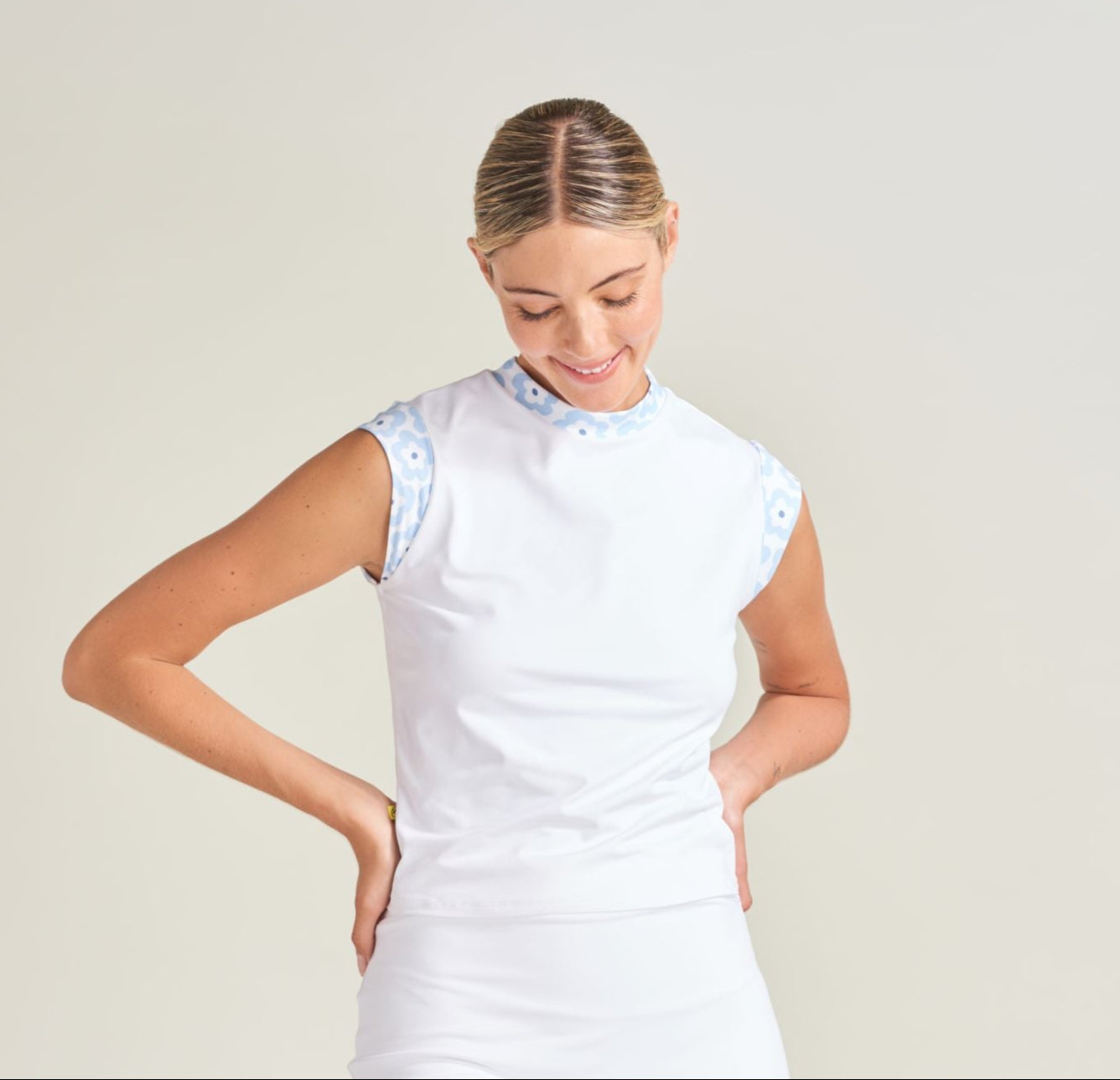 Woman tennis athlete wearing white tennis t-shirt with flower print contrast fabric on cap sleeves and mock neck.
