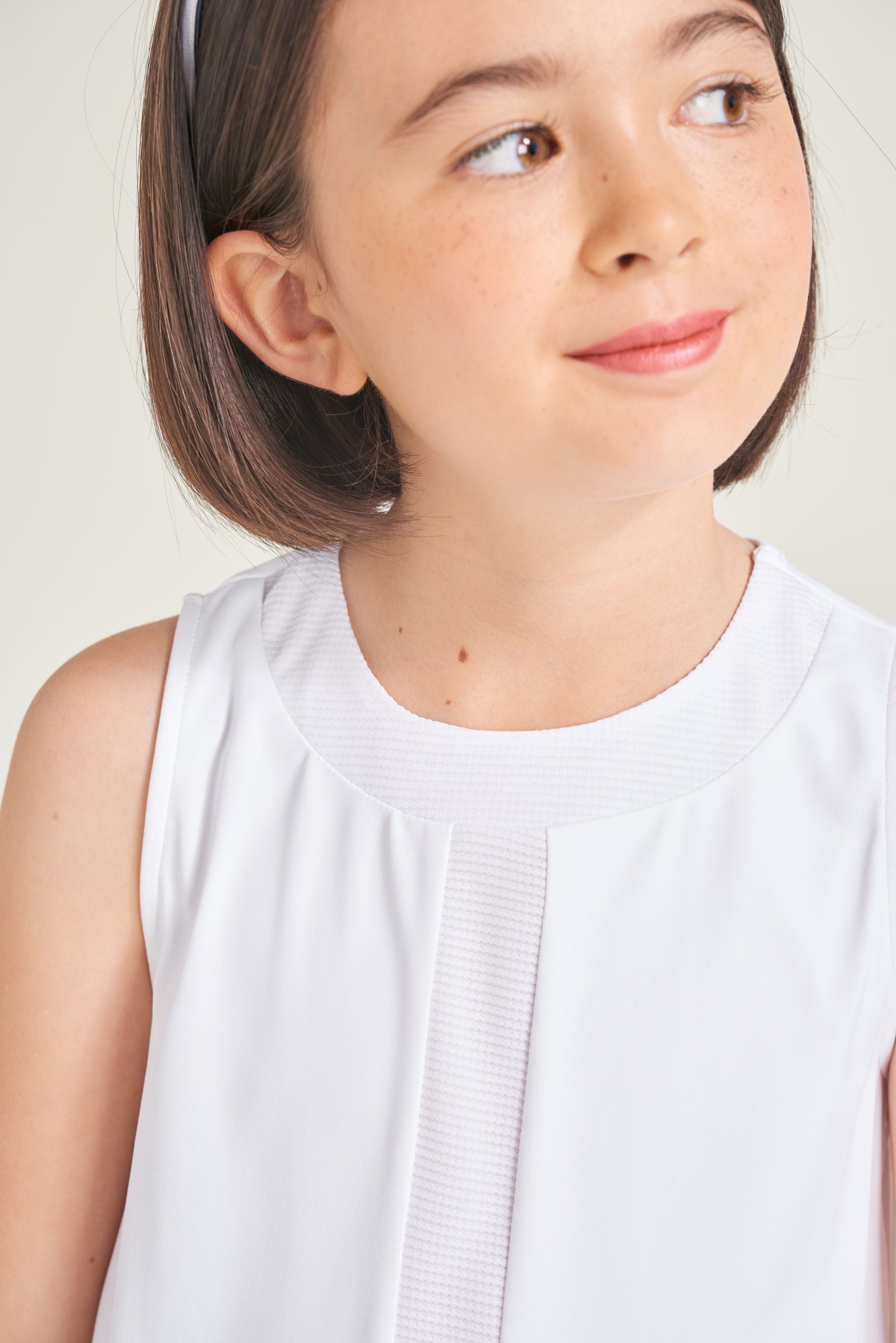 Detail view of youth girl tennis athlete wearing white tennis dress with contrast strip down center front and neckline.