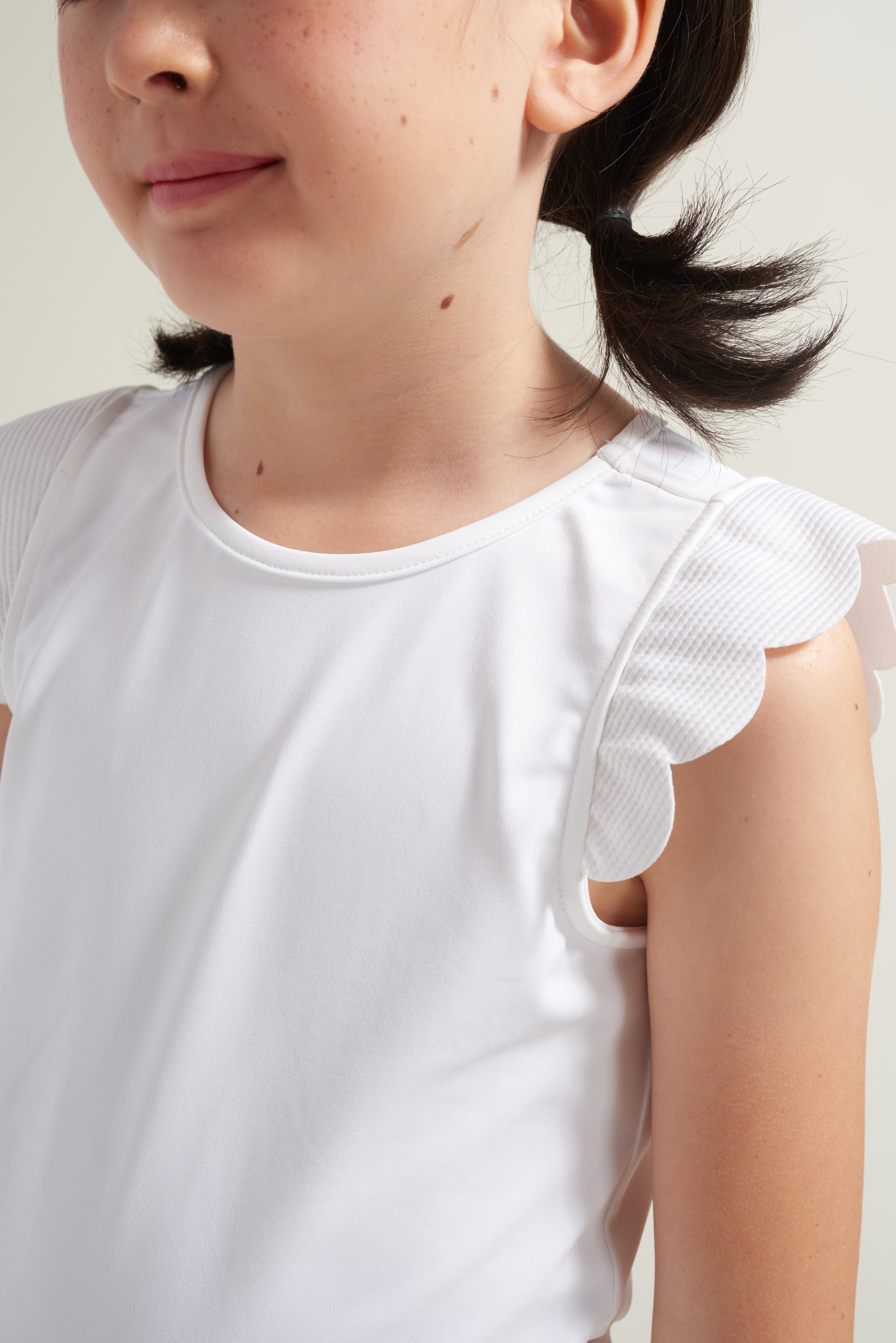 Detail view of all white tennis t-shirt for girls with scalloped arm detail.