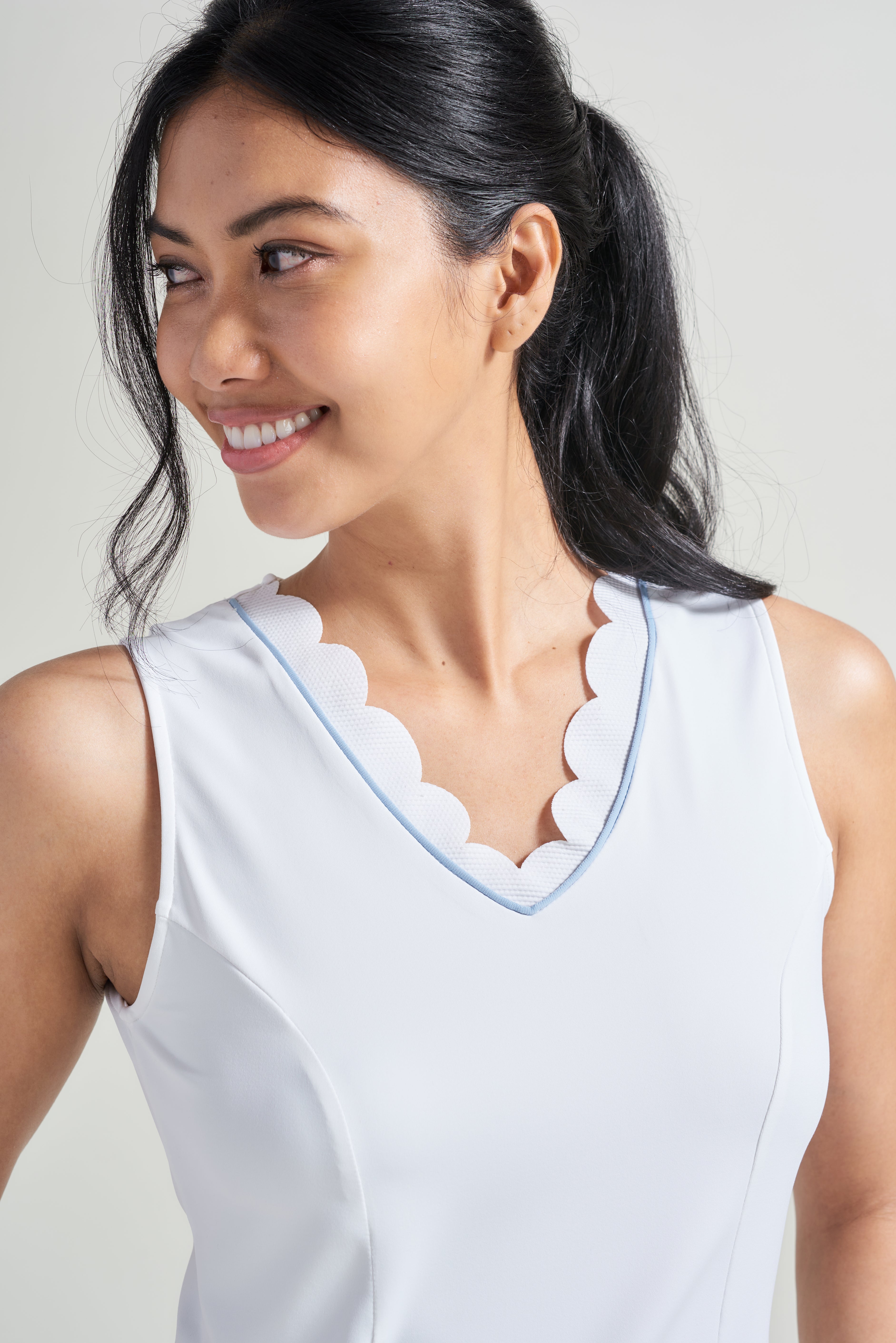 Detail view of white tennis v-neck shirt for women with scalloped neckline and blue accent.