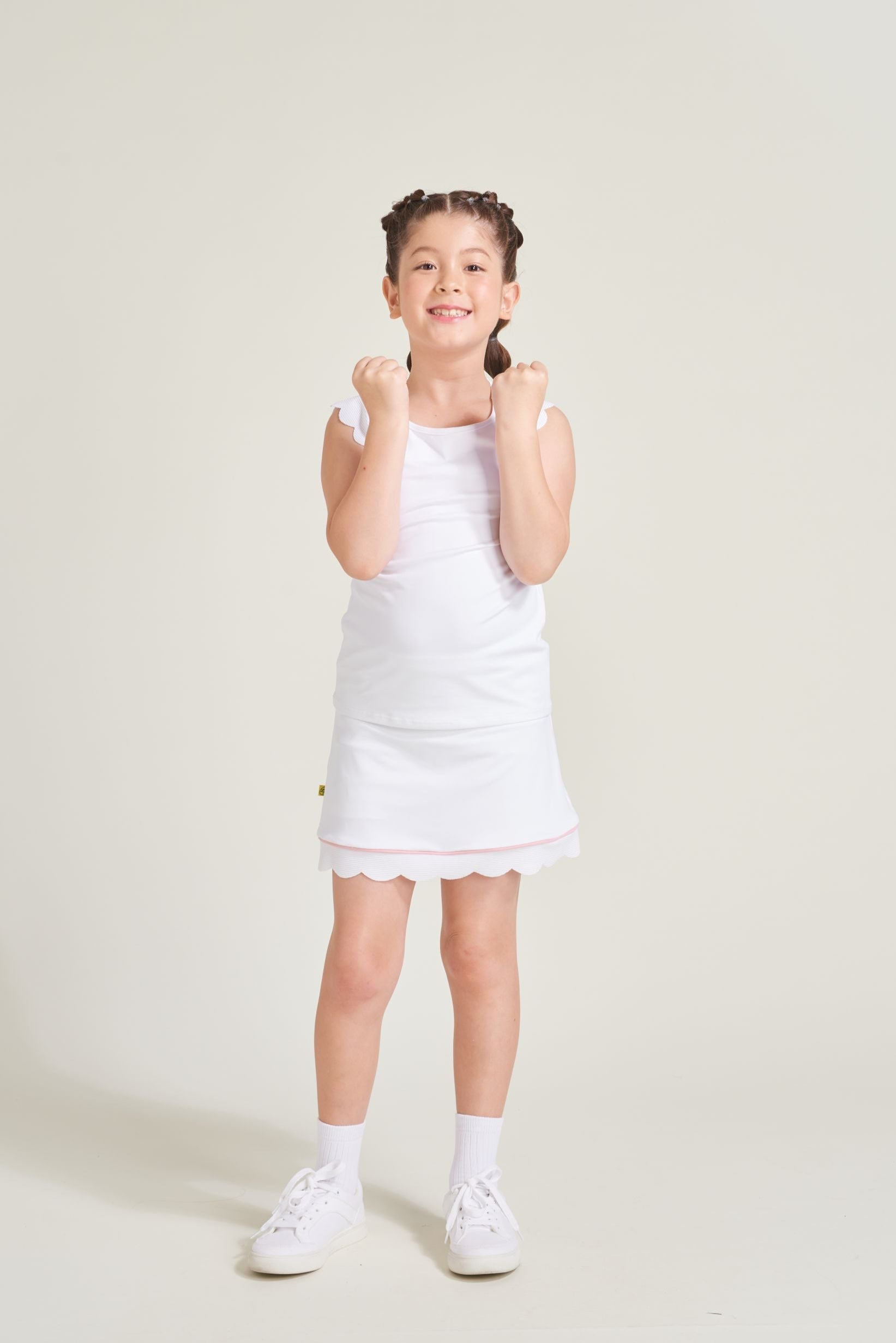 Youth girls' tennis player wearing white tennis skort with pink accents and scalloped hem.