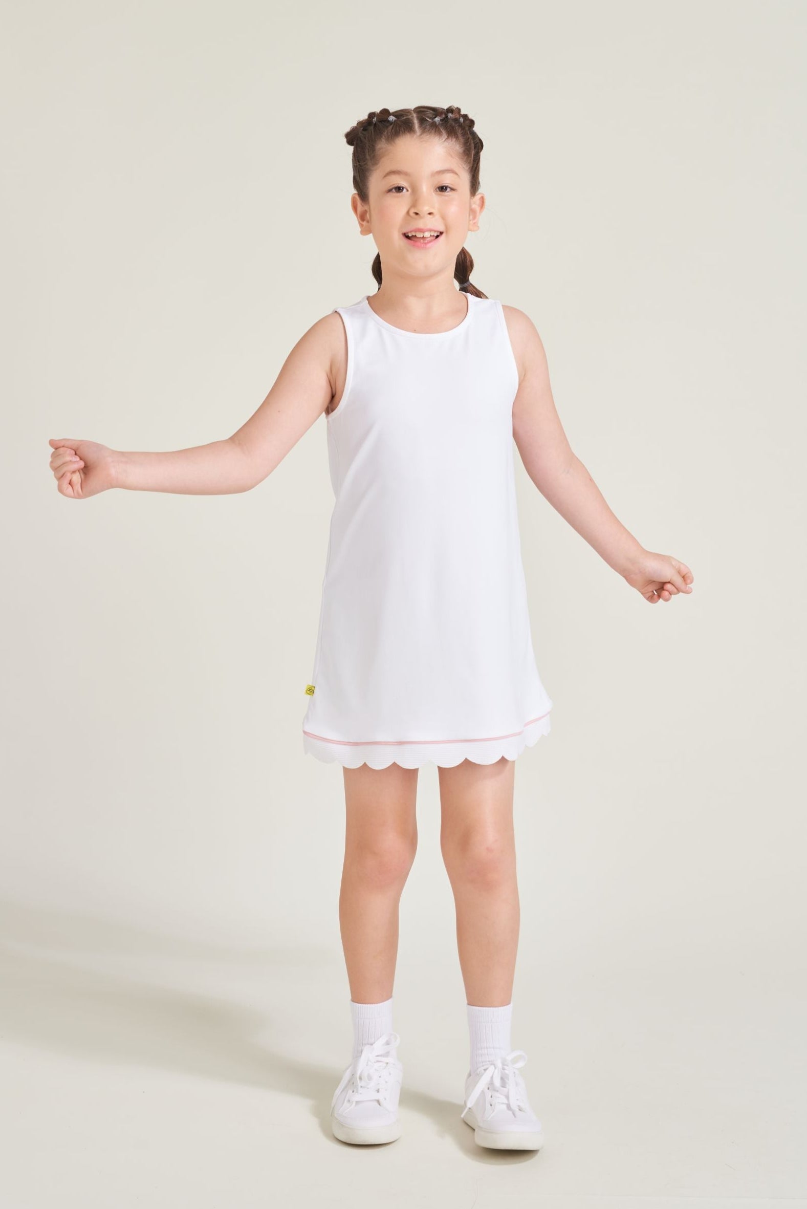 Youth girls' tennis athlete wearing a white tennis dress with pink accent and scalloped hem.