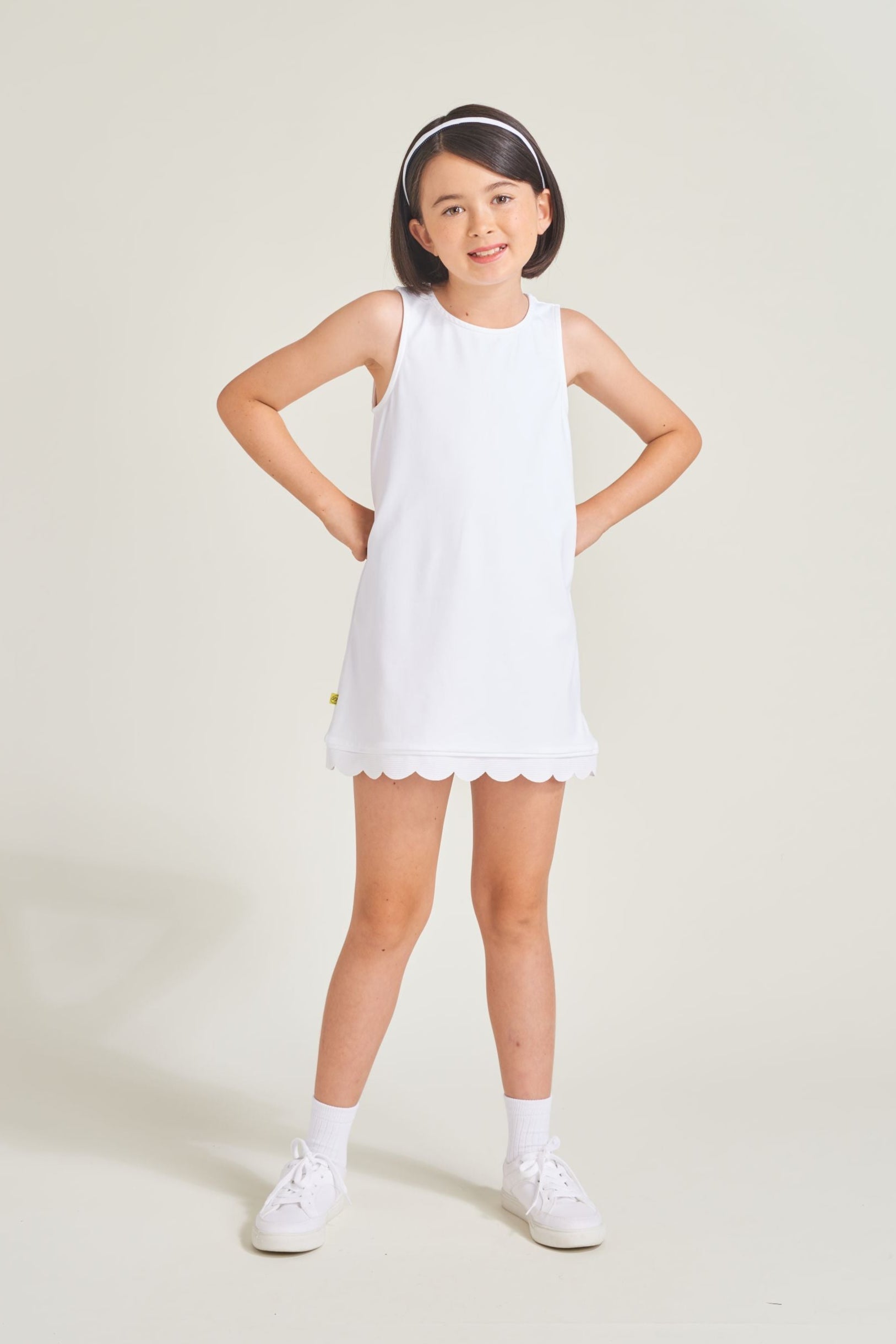 Youth girls' tennis player wearing an all-white tennis shift dress with scalloped hem.