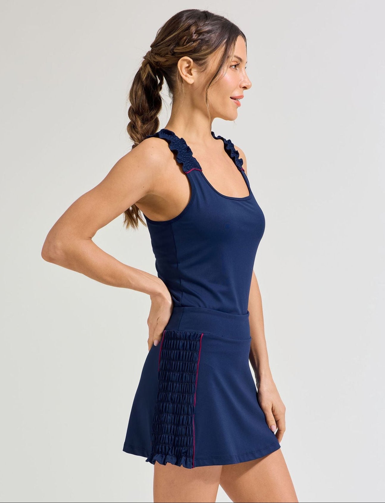 Women's navy tennis outfit. Navy tennis skort with smocking side panel. and burgundy trim. Also wearing matching tennis tank top with burgundy trim and smocking straps.