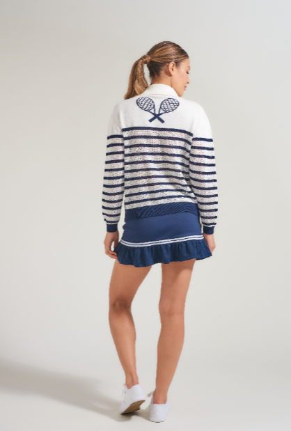 Back view of female tennis player in tennis sweater with tennis racquet design in white and navy. Woman is also wearing matching navy tennis skort with navy and white trim.