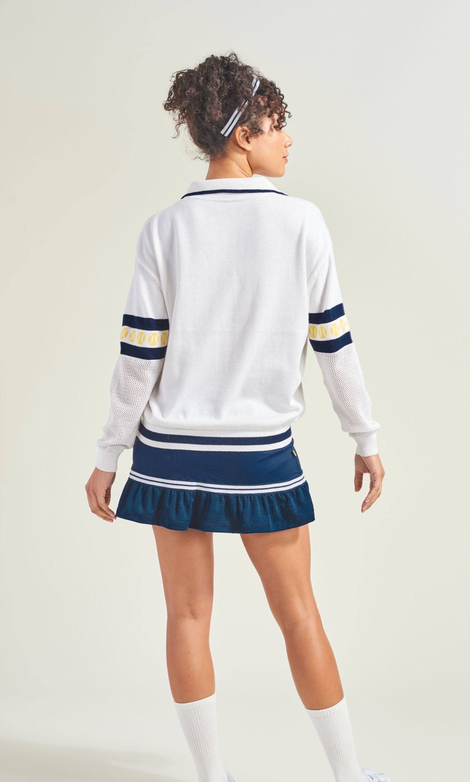 Person wearing a white sweater with navy and yellow accents and a blue skirt on a plain background