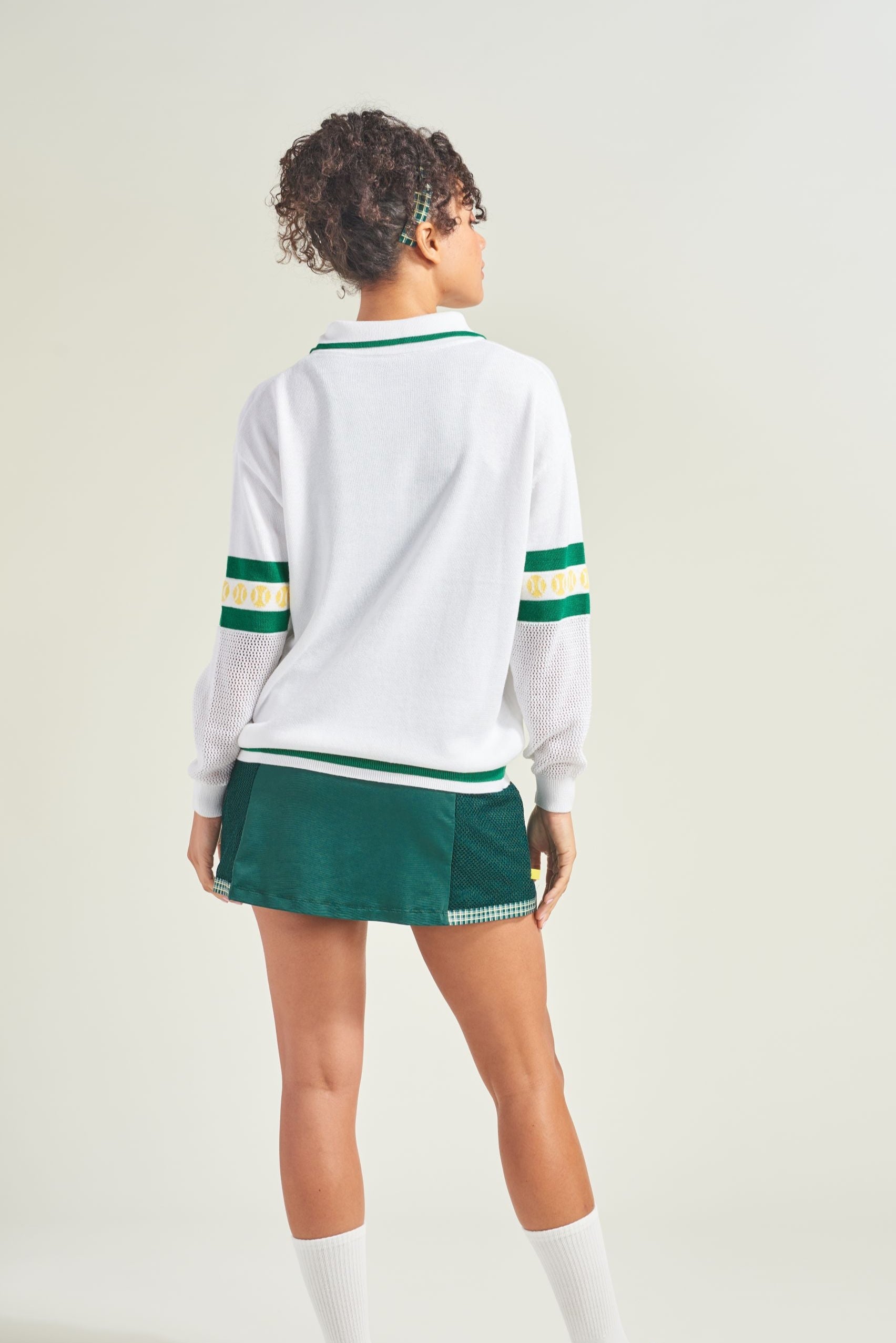 Person wearing a white sweater with green accents and a green skirt on a light background