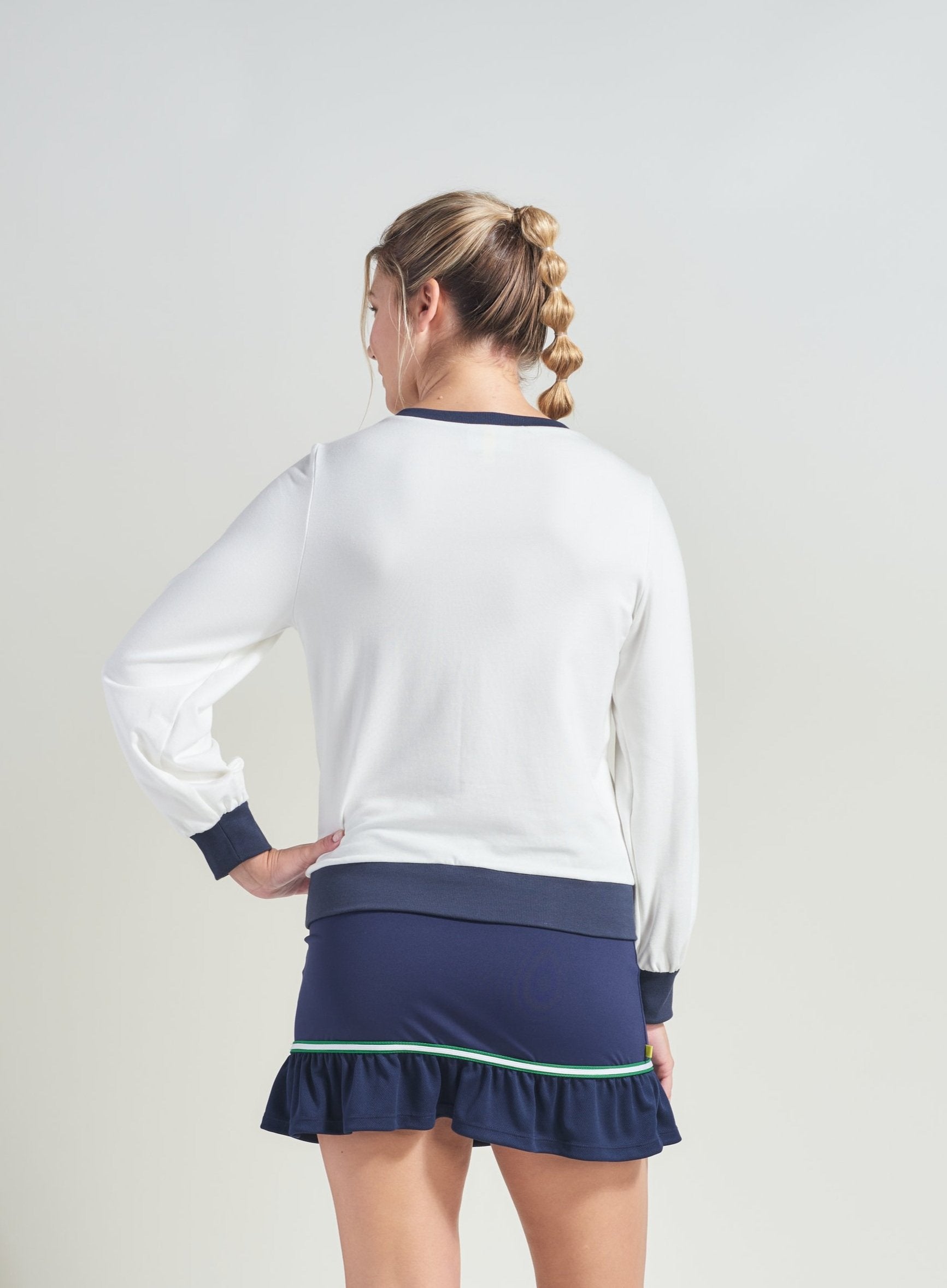 Back view of women's tennis lifestyle uniform. Woman is wearing white sweatshirt with navy accents and matching navy tennis skort.