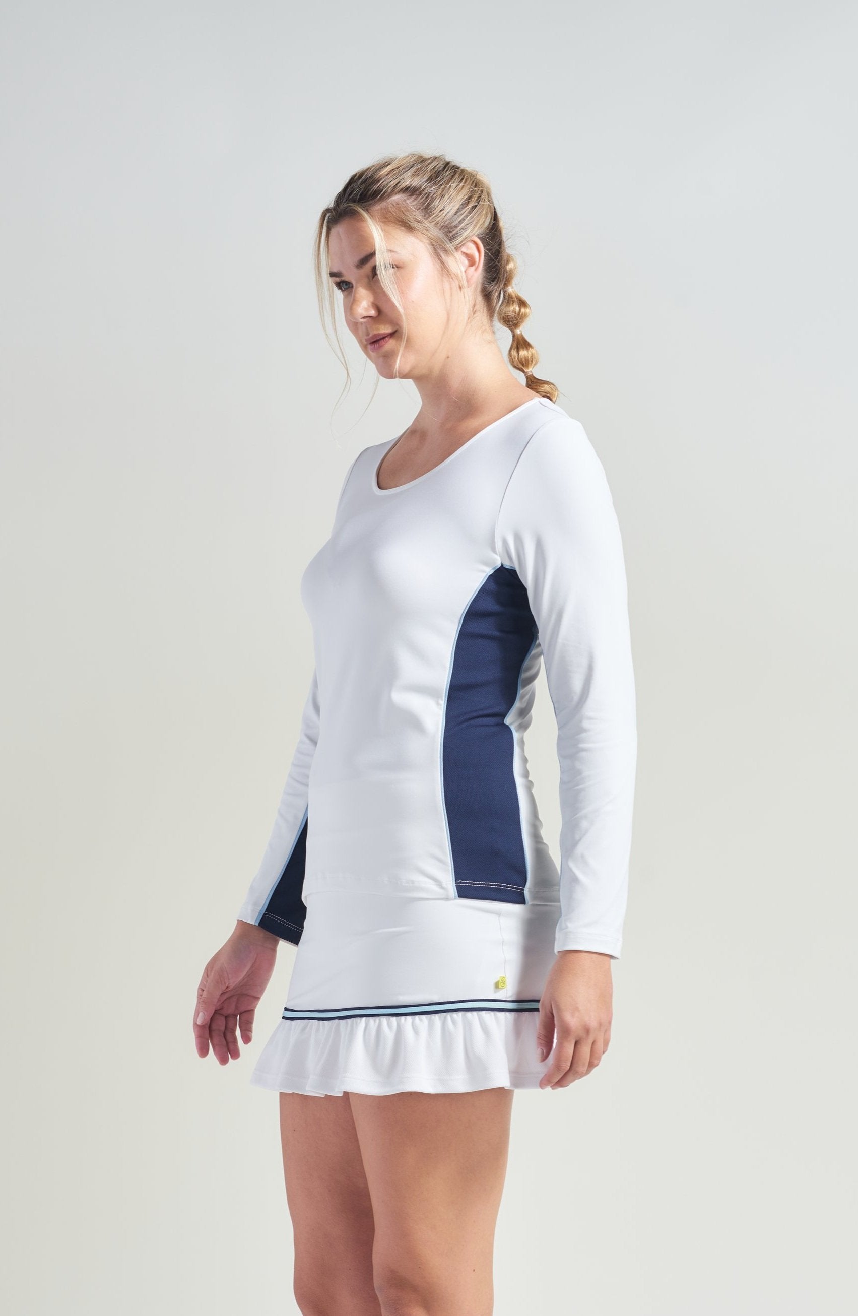 Tennis athlete wearing white women's workout shirt with navy color block. Woman is also wearing a white tennis skort.