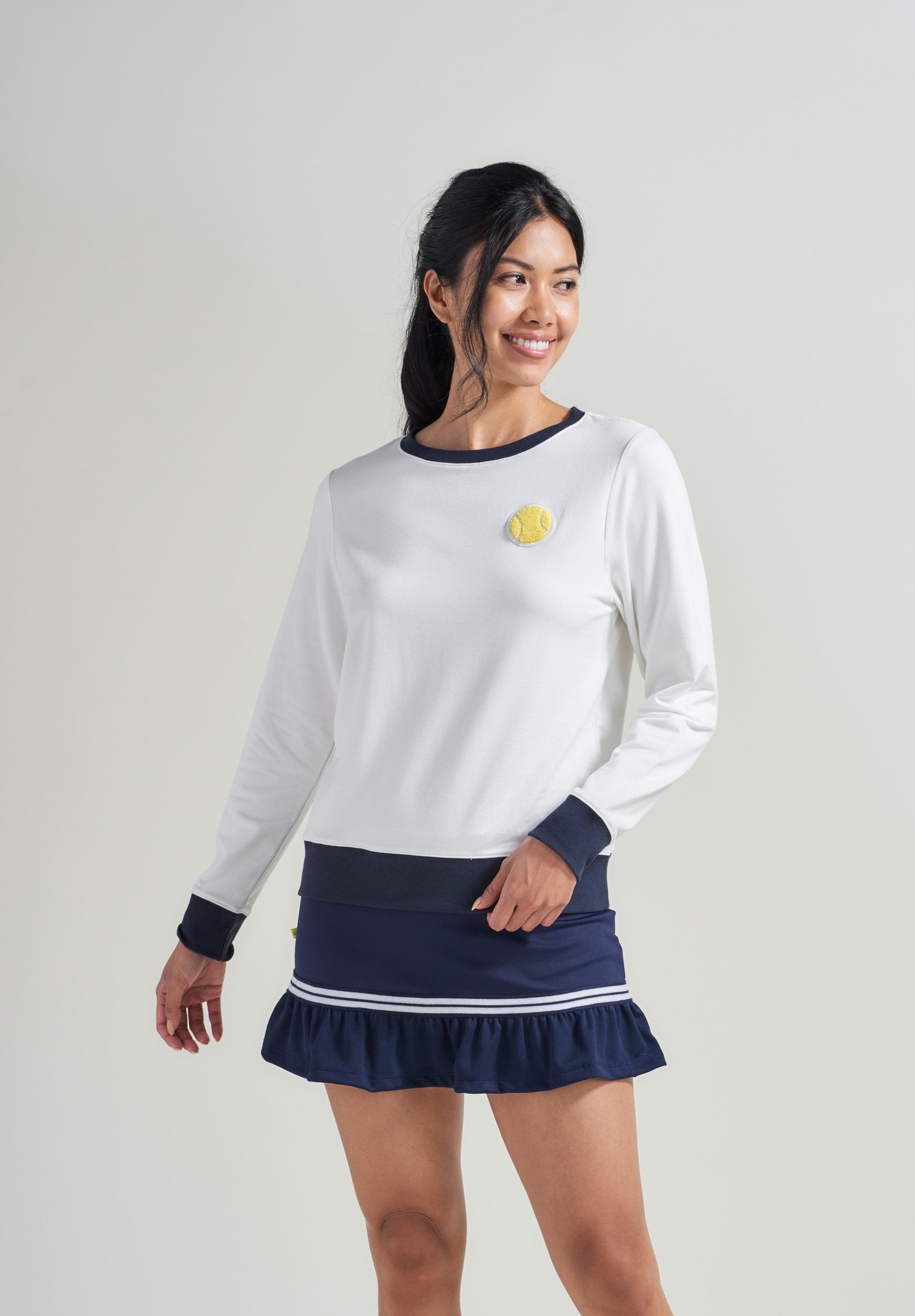 Woman tennis player in navy ribbed cuff, neckline and hem with tennis embroidery patch. Woman is also wearing matching navy tennis skort.