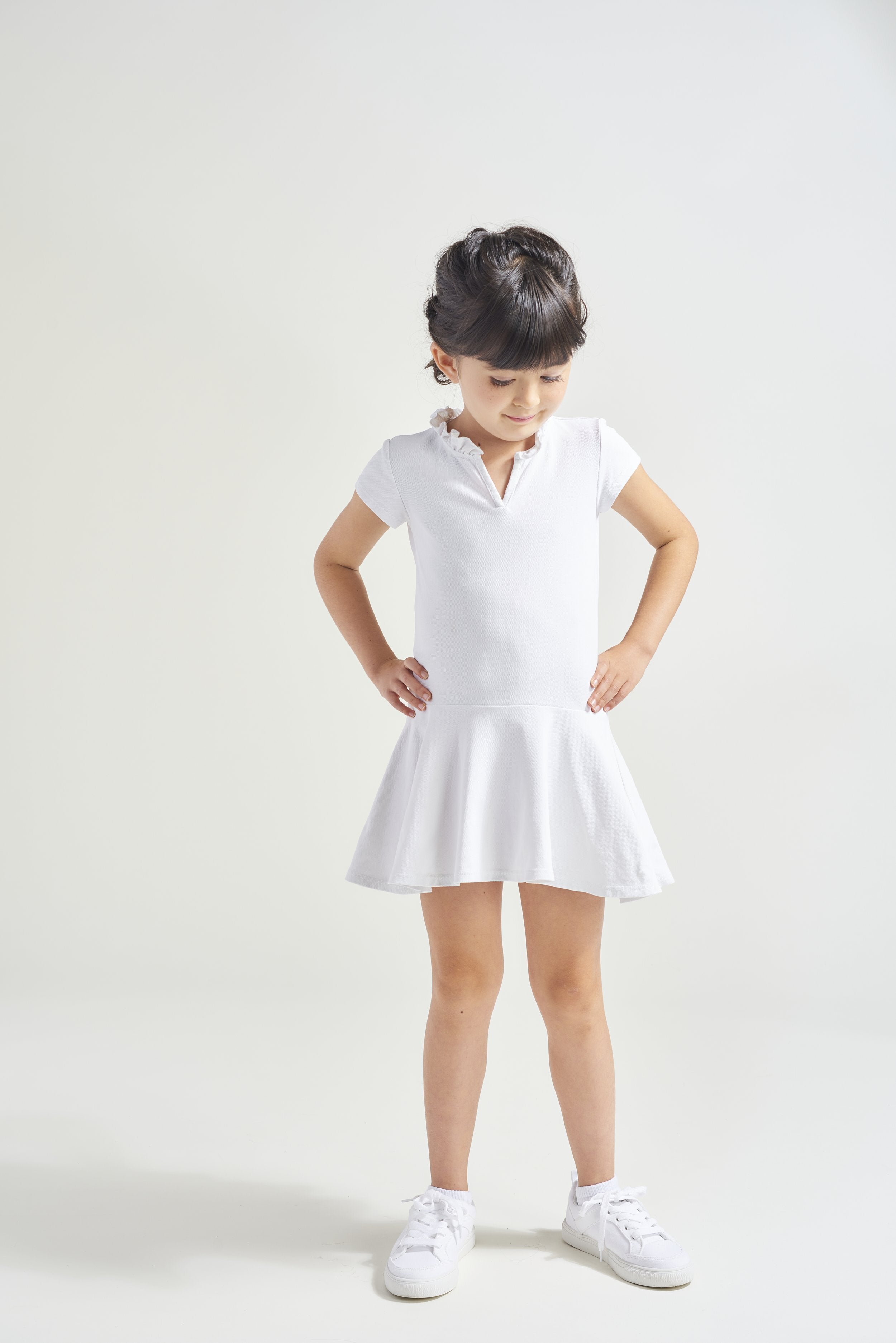 Youth girl is wearing white tennis dress with short sleeves and ruffled neckline.
