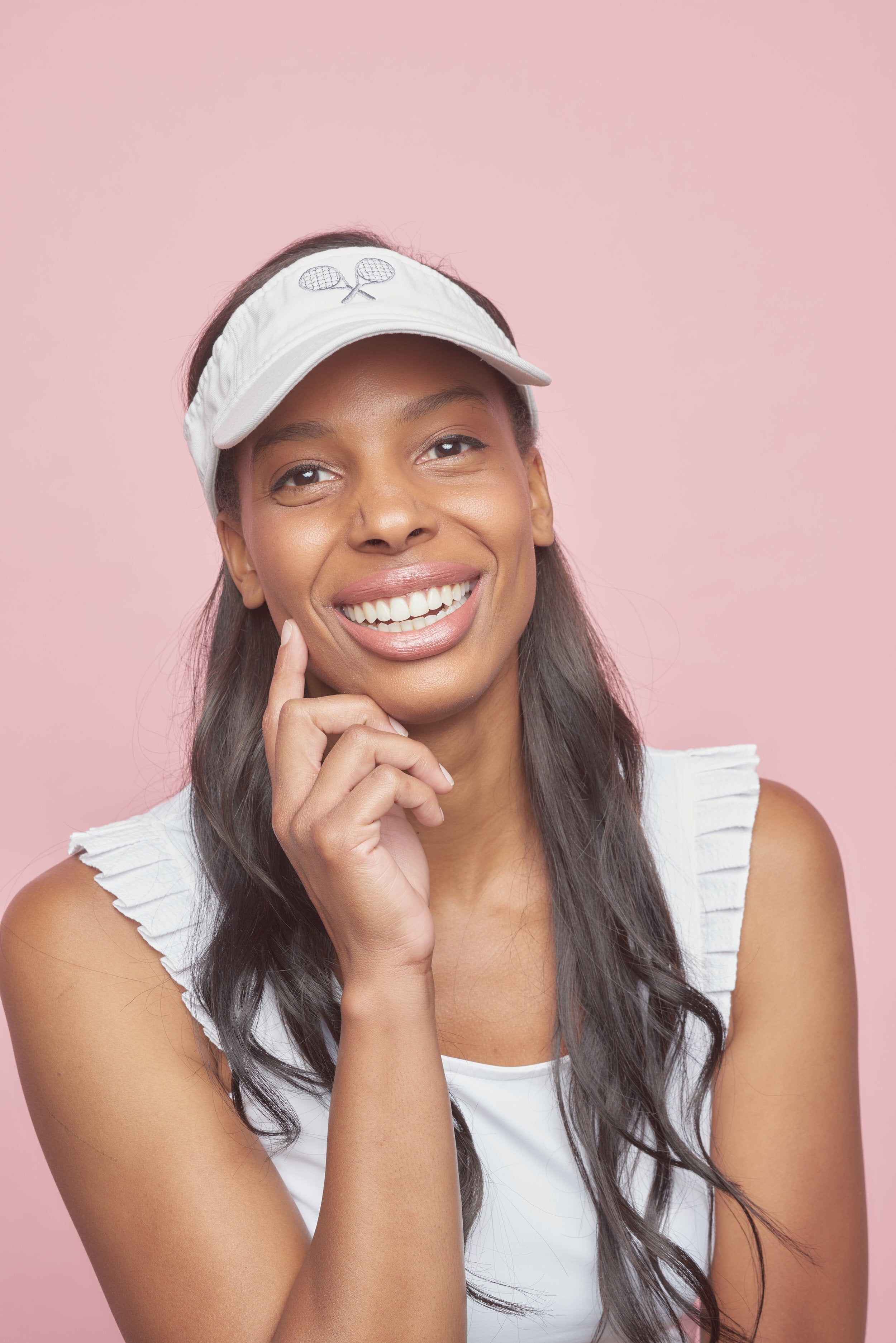 Female tennis player in white women's tennis visor. Woman is also wearing women's tennis tank top with pleated sleeves.