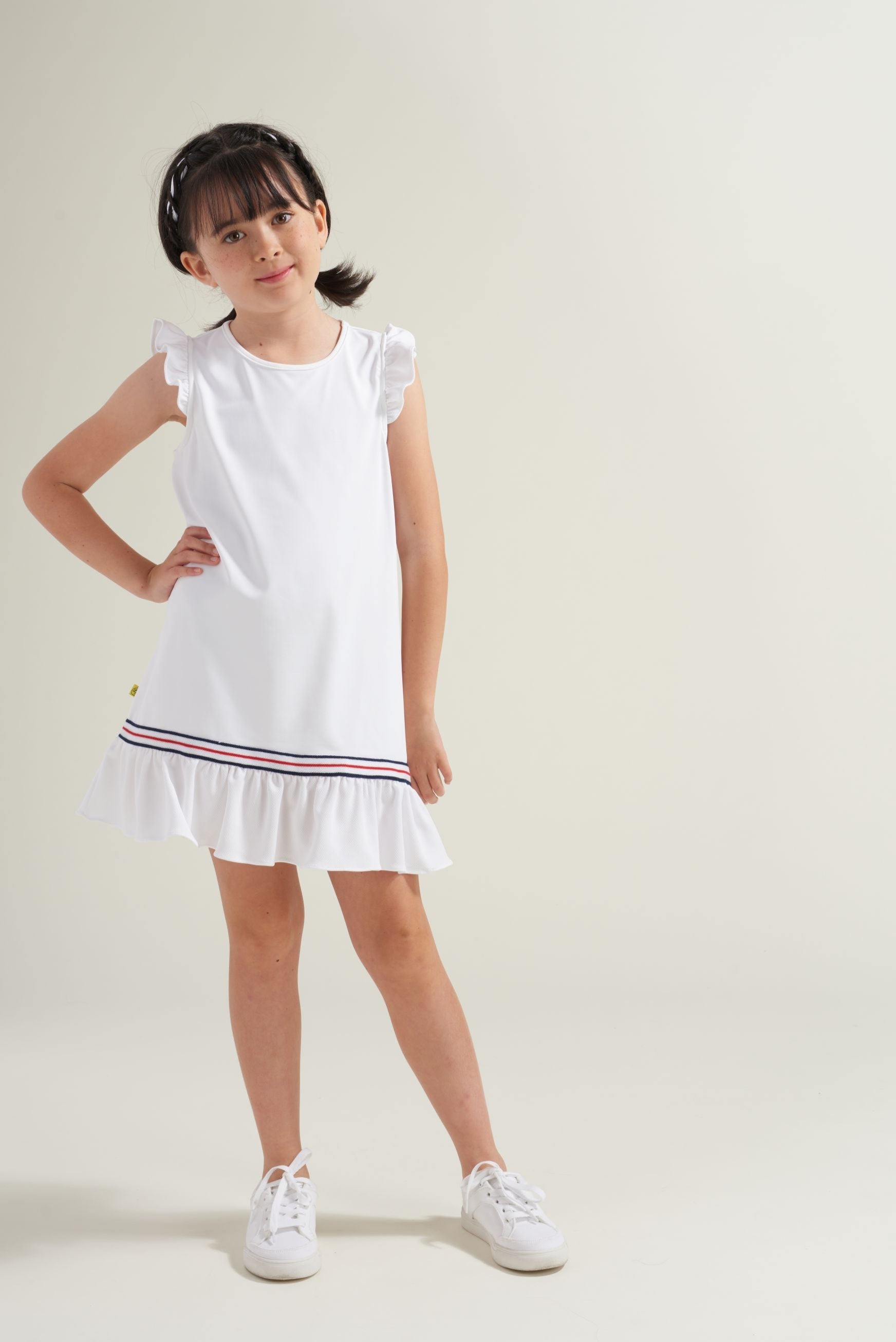 Young girl wearing a white dress with a red and blue trim on a plain background