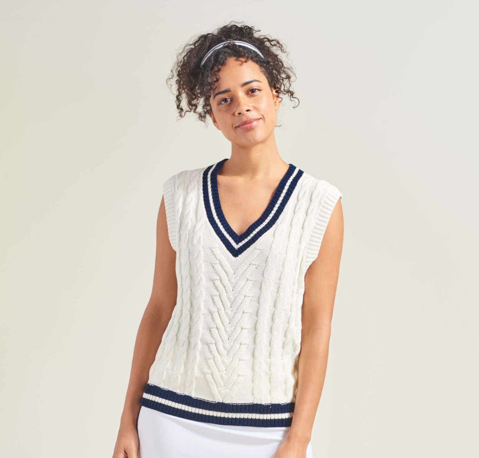Woman wearing a white and navy sports outfit on a plain background