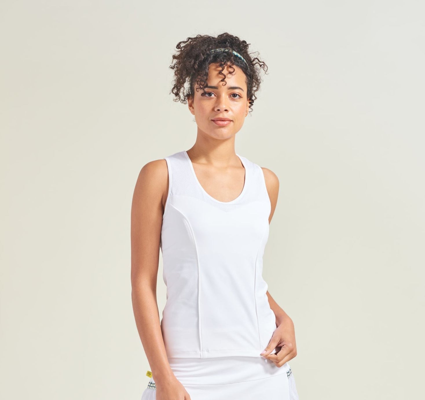 Woman wearing a white sleeveless top and skirt with white socks on a light background