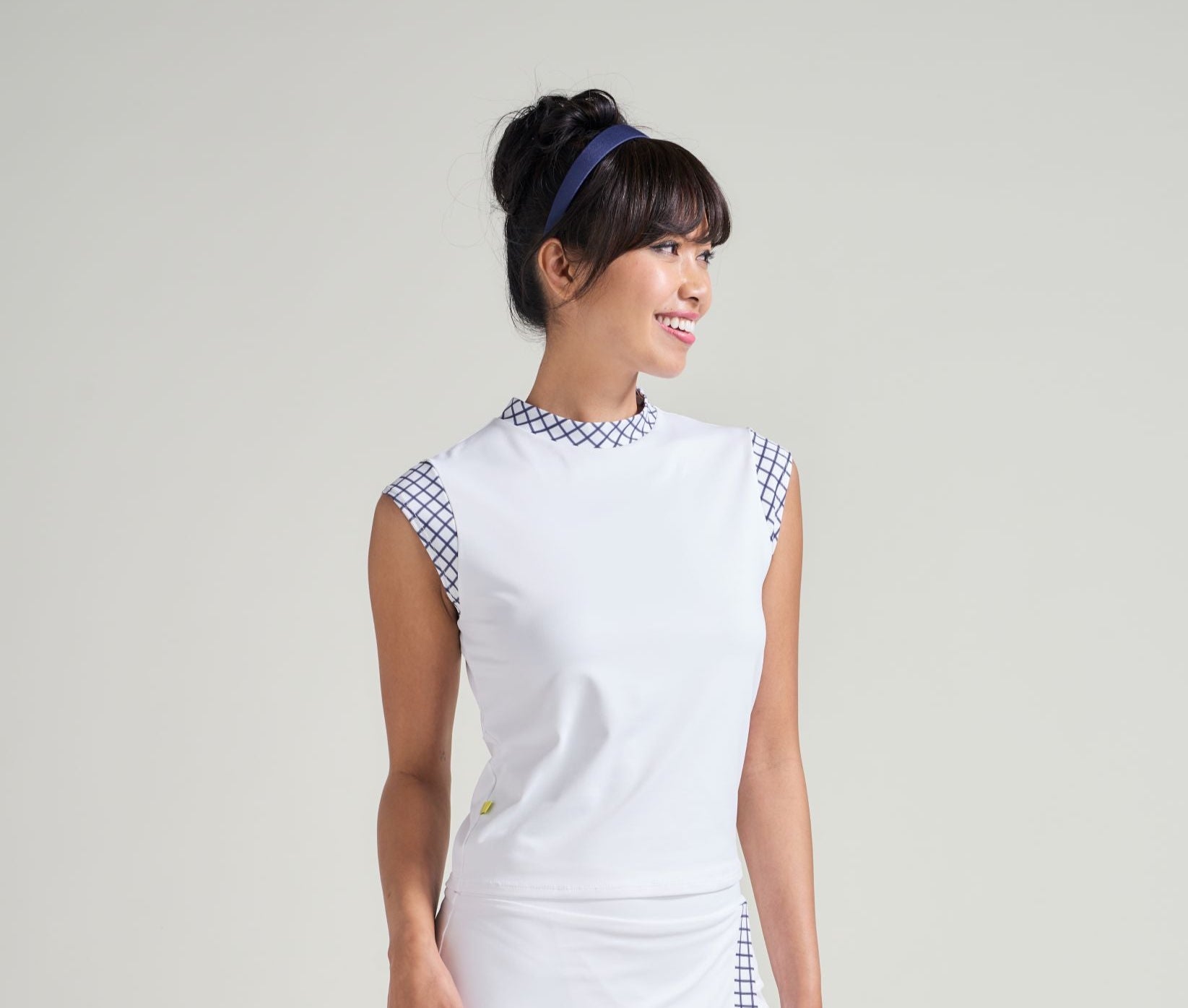 Woman wearing a white dress with blue checkered details on a plain background