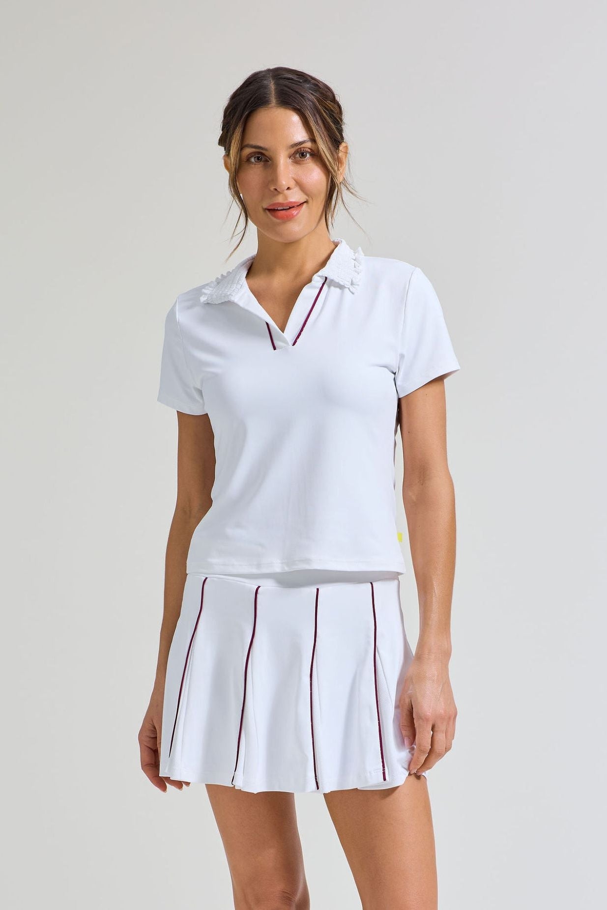 Women's tennis player wearing white tennis skort with burgundy trim and white tennis polo shirt with matching burgundy trim.