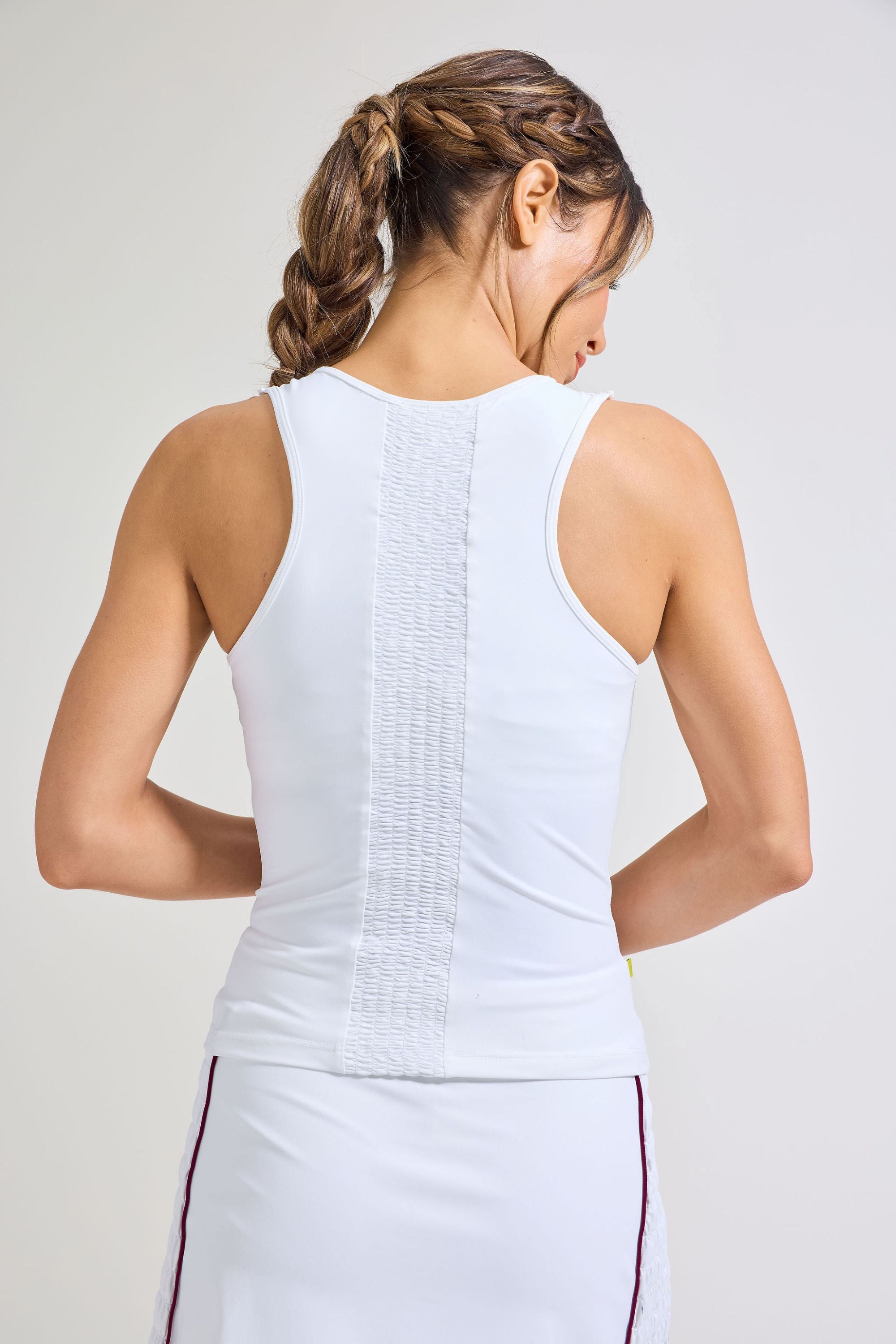 Back view of women's white tennis tank top with smocking panel down the center. Also wearing matching white tennis skort. 